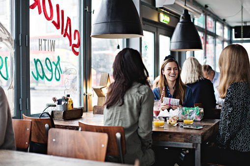 Smiling female friends enjoying while sitting at dining table for brunch in restaurant | Photo: Getty Images