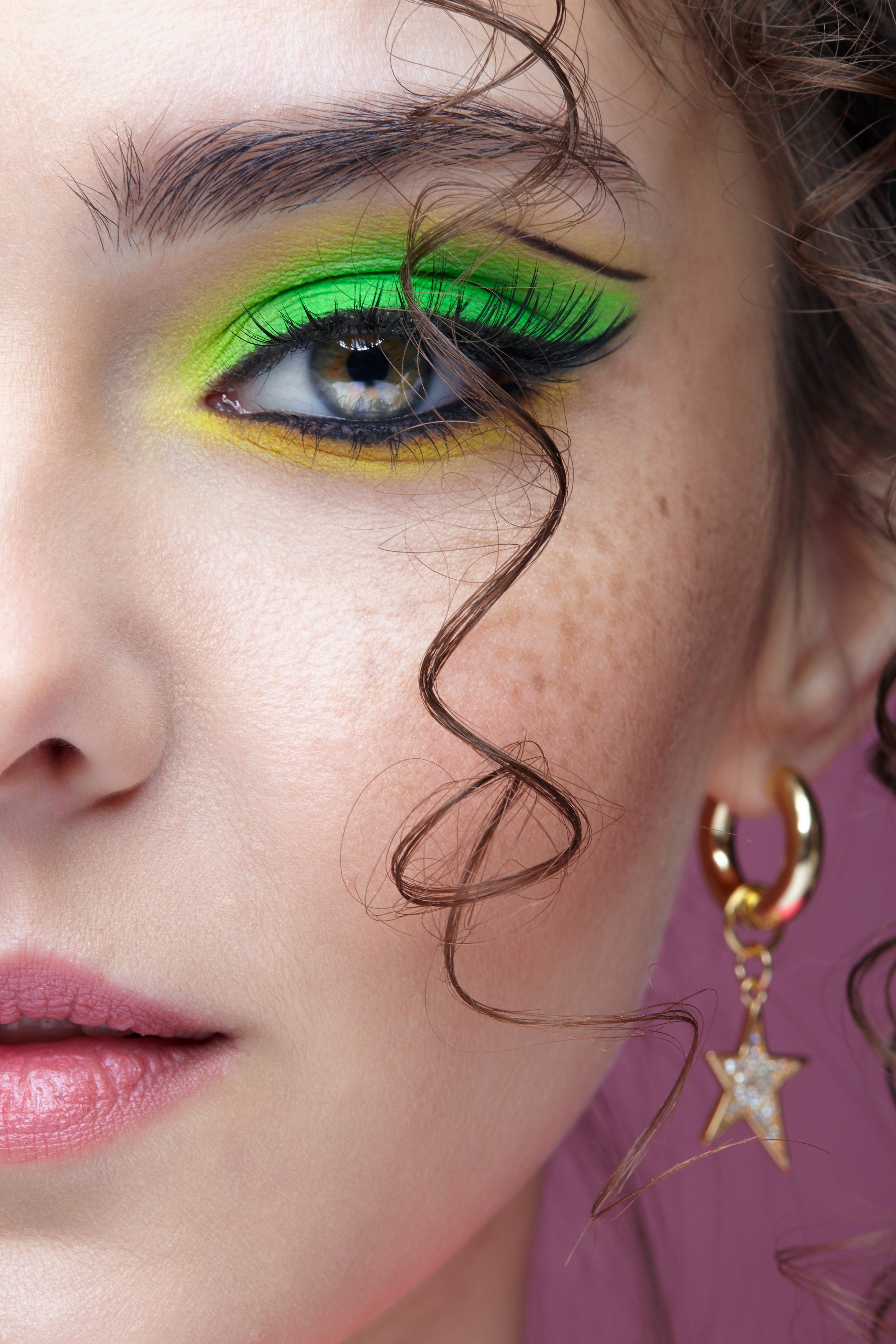 A portrait of a young woman with unusual green eyes, makeup, curly hair, and earrings, against a pink background | Source: Shutterstock