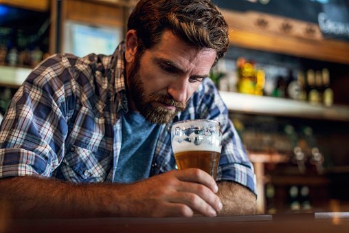 Sad man pictured looking at beer glass while sitting in beer bar | Photo: Getty Images