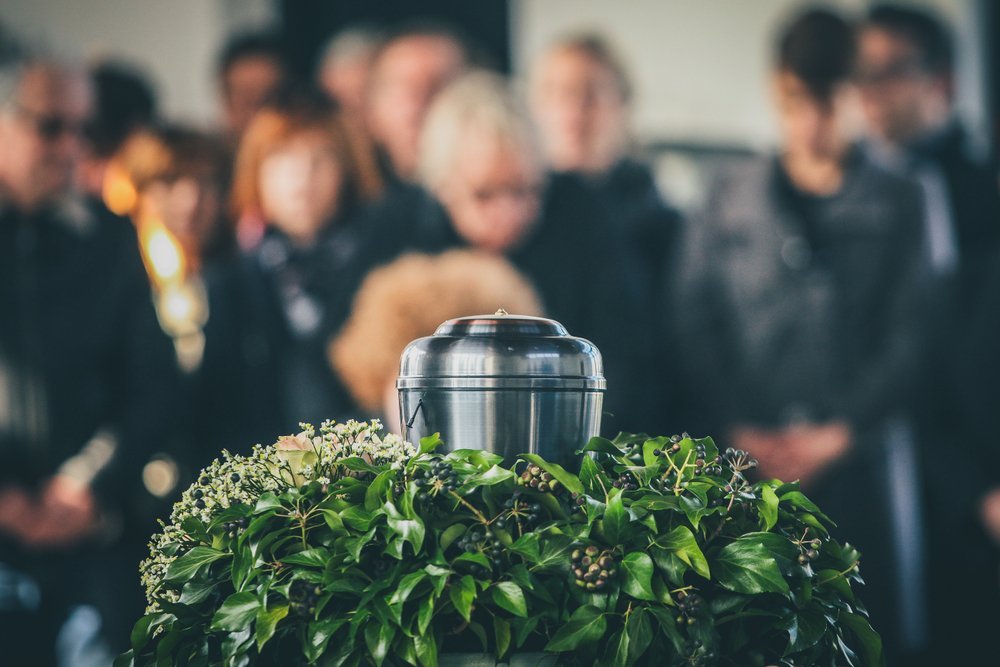 A metal urn with ashes of a dead person on a funeral, with people mourning in the background on a memorial service | Photo: Shutterstock