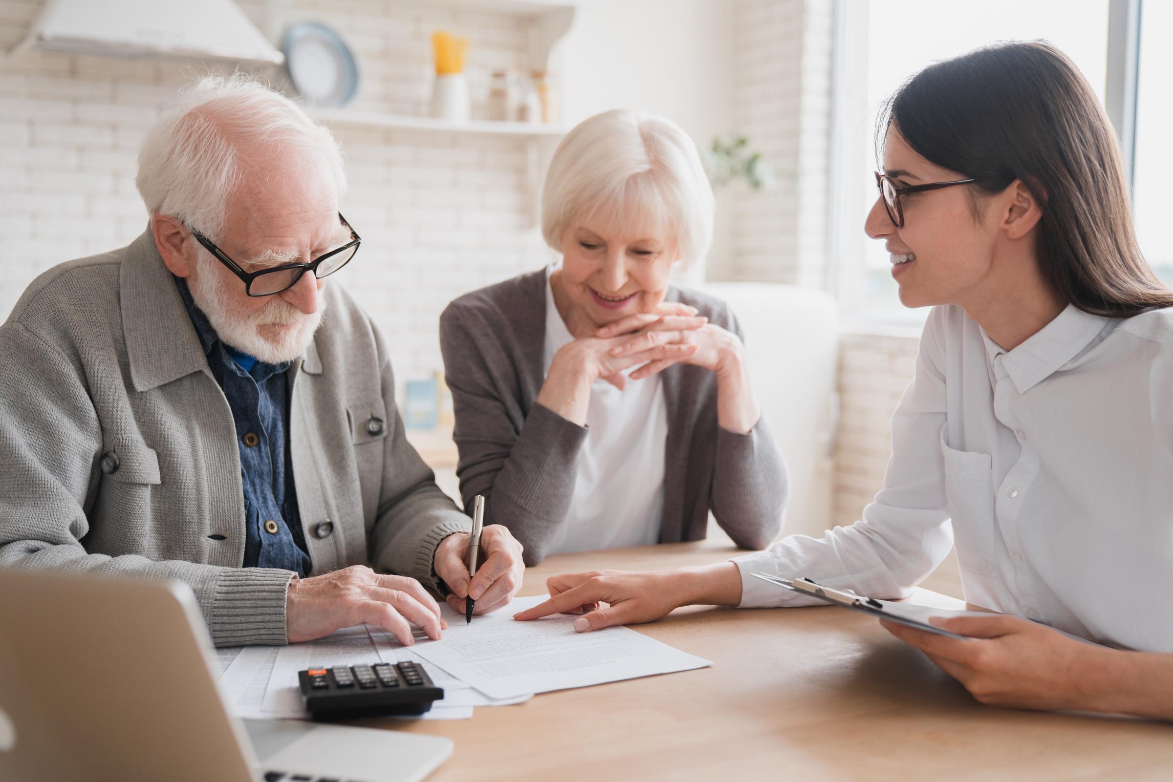 An older couple signing a document while a younger woman facilitates | Source: Shutterstock