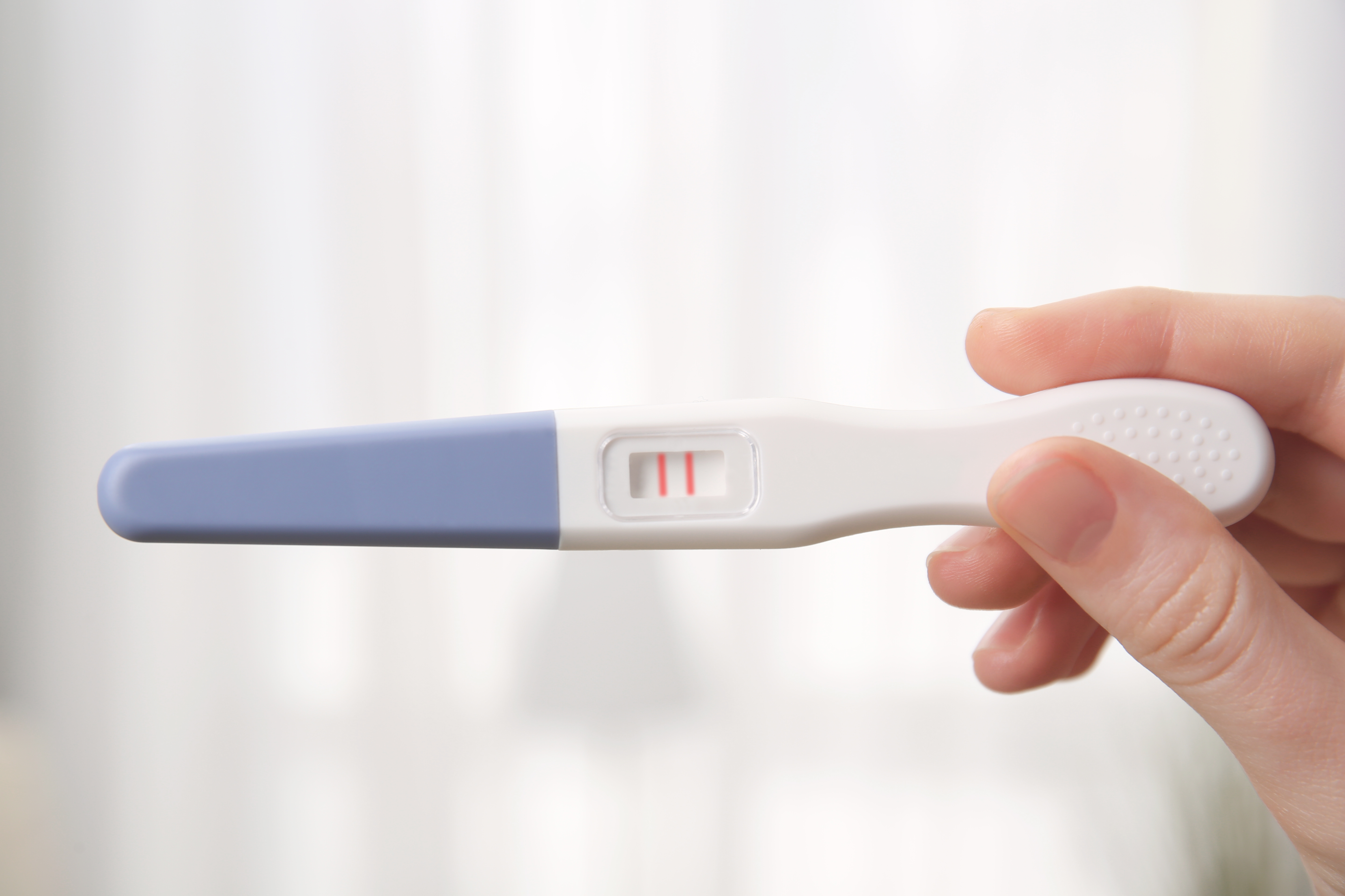 Pregnancy test in female hand on blurred background. | Source: Shutterstock