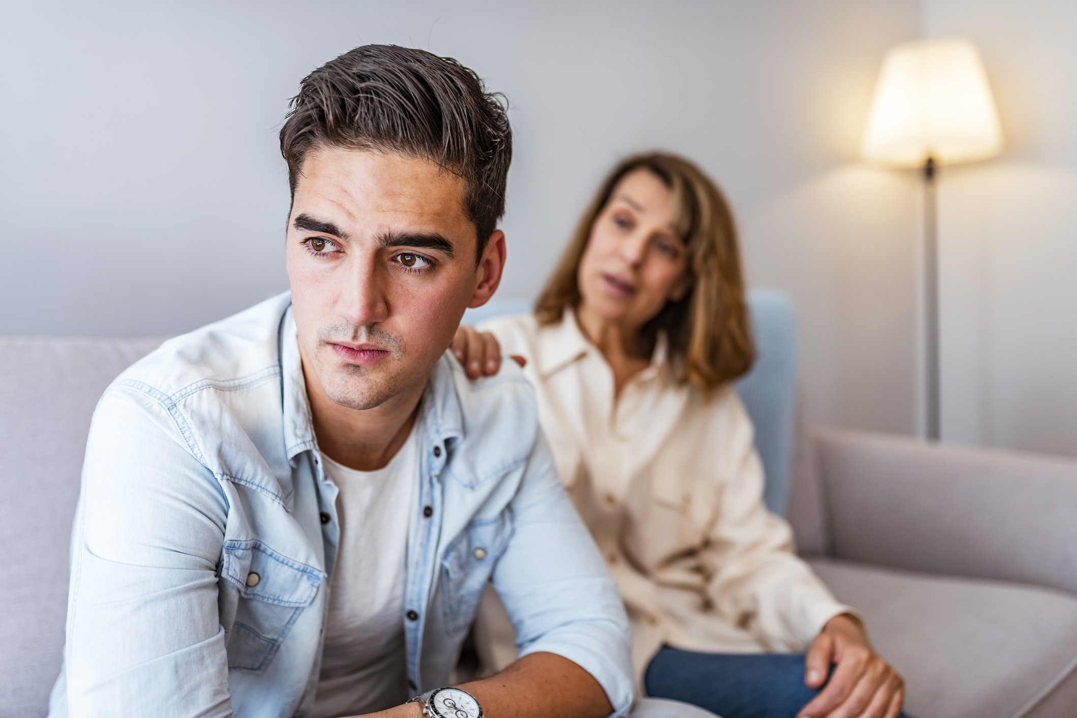 Frustrierte Mutter im Gespräch mit ihrem verärgerten Sohn, der auf der Couch sitzt | Quelle: Getty Images