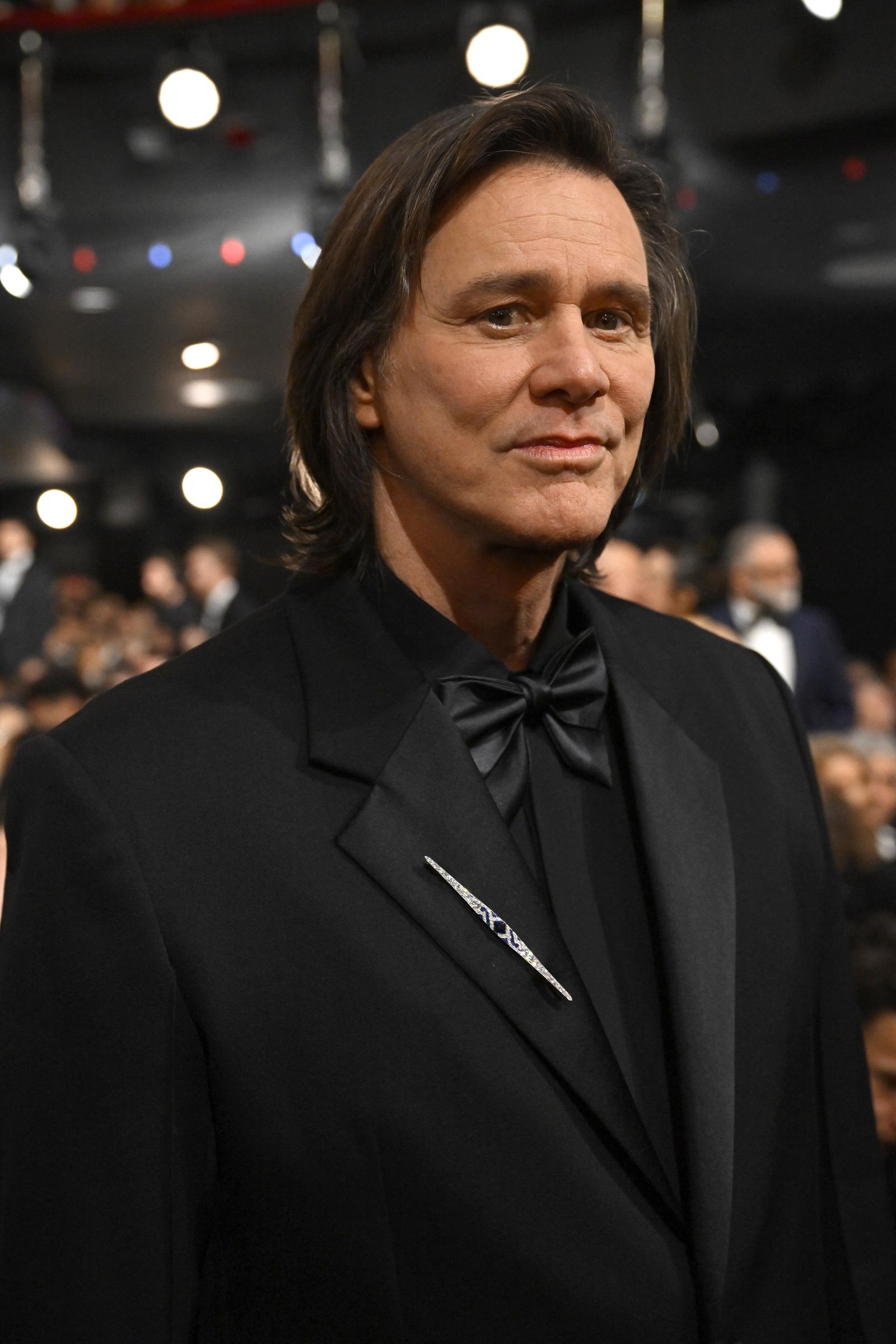 Dressed in a sharp black tuxedo with a satin bow tie, Jim Carrey exudes understated elegance. A sleek lapel pin adds a subtle gleam against the monochrome ensemble as soft stage lights glow behind him. He attends the 51st César Film Awards at L'Olympia in Paris, France.