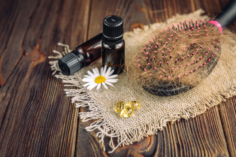 Peine con cabello y aceites esenciales, manzanilla y cápsulas de vitaminas en un fondo de madera oscura. Fuente: Shutterstock
