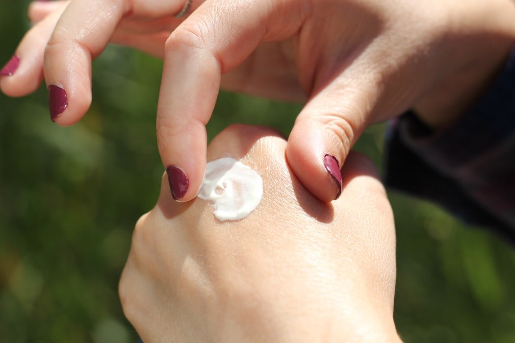 Une femme appliquant de la crème sur la peau de ses mains. l Source : Unsplash
