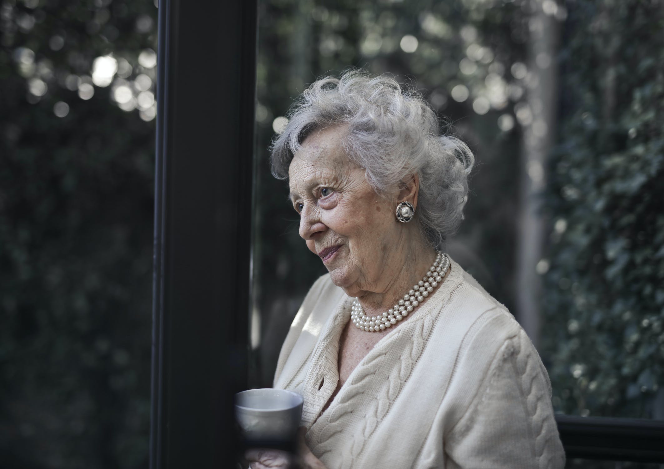 Una anciana mirando hacia el horizonte mientras toma una bebida. | Foto: Pexels