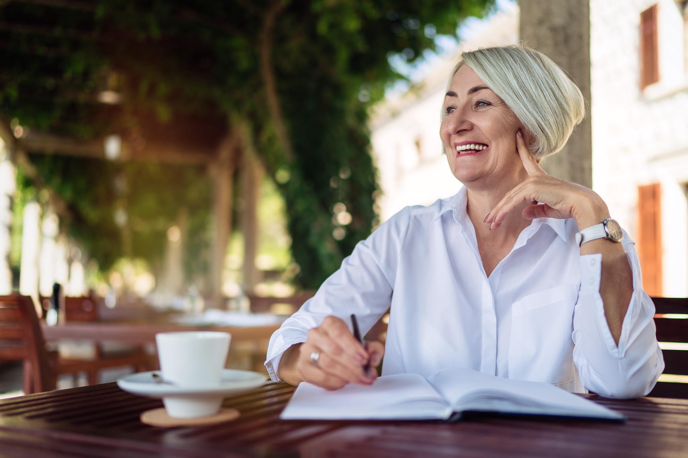 Happy senior woman writing to notebook or diary at a café | Source: Shutterstock