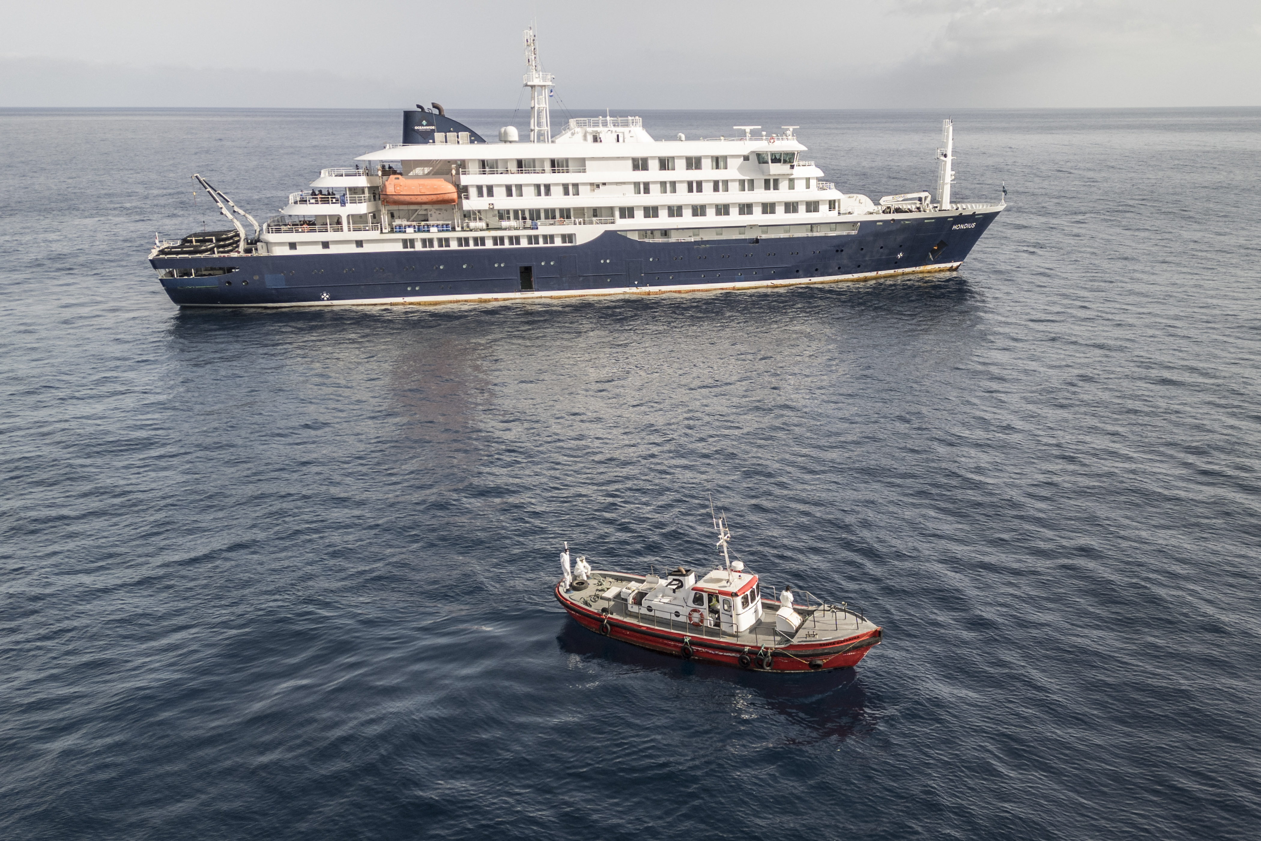 An aerial view of an ambulance boat carrying crew members wearing hazmat suits as they approach the pilot door on the starboard side of the cruise ship MV Hondius, while stationary off the port of Praia, the capital of Cape Verde, on May 5, 2026 | Source: Getty Images