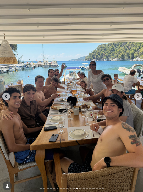 A large group sat around a long table at a waterfront restaurant. Boats and a tree-covered shoreline were visible behind them. | Source: Instagram/katehudson