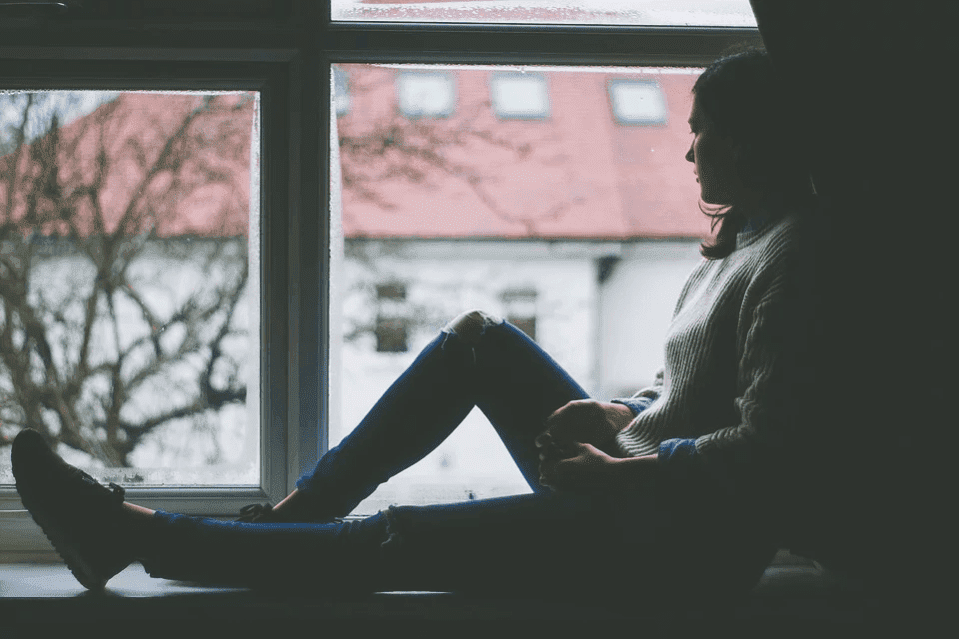 A woman sitting by a window and being worried| Photo: Pixabay
