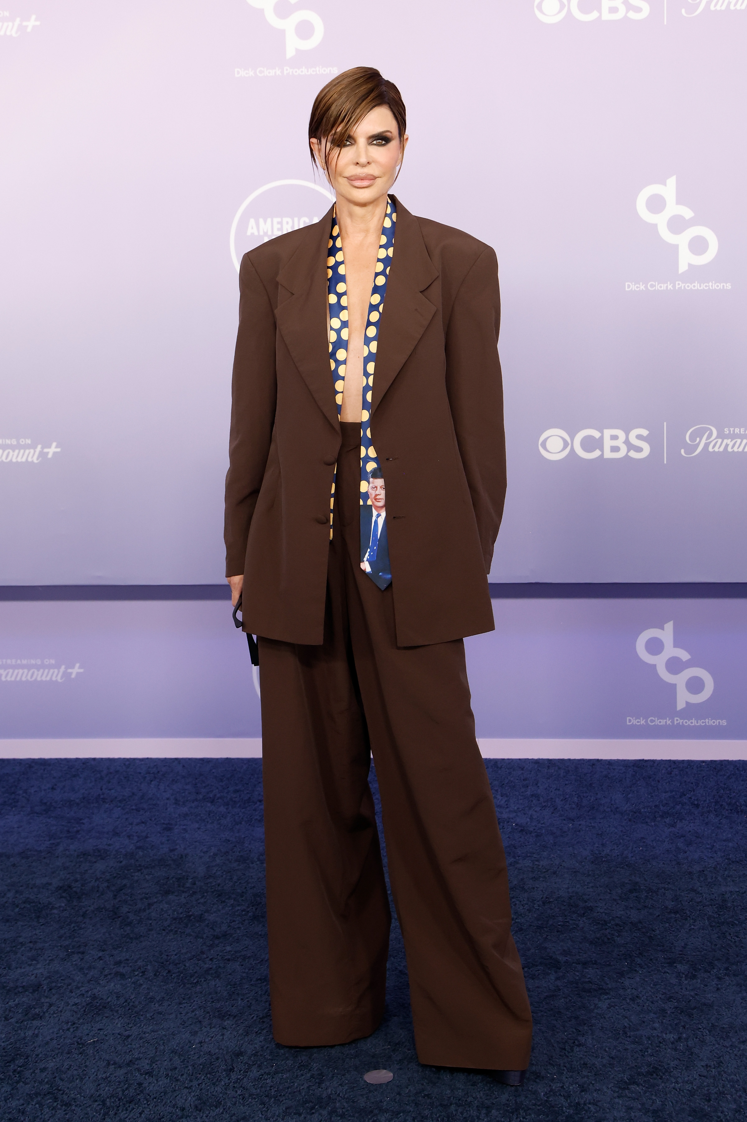 Lisa Rinna keeps one hand in her pocket while posing beneath the purple-lit American Music Awards backdrop | Source: Getty Images
