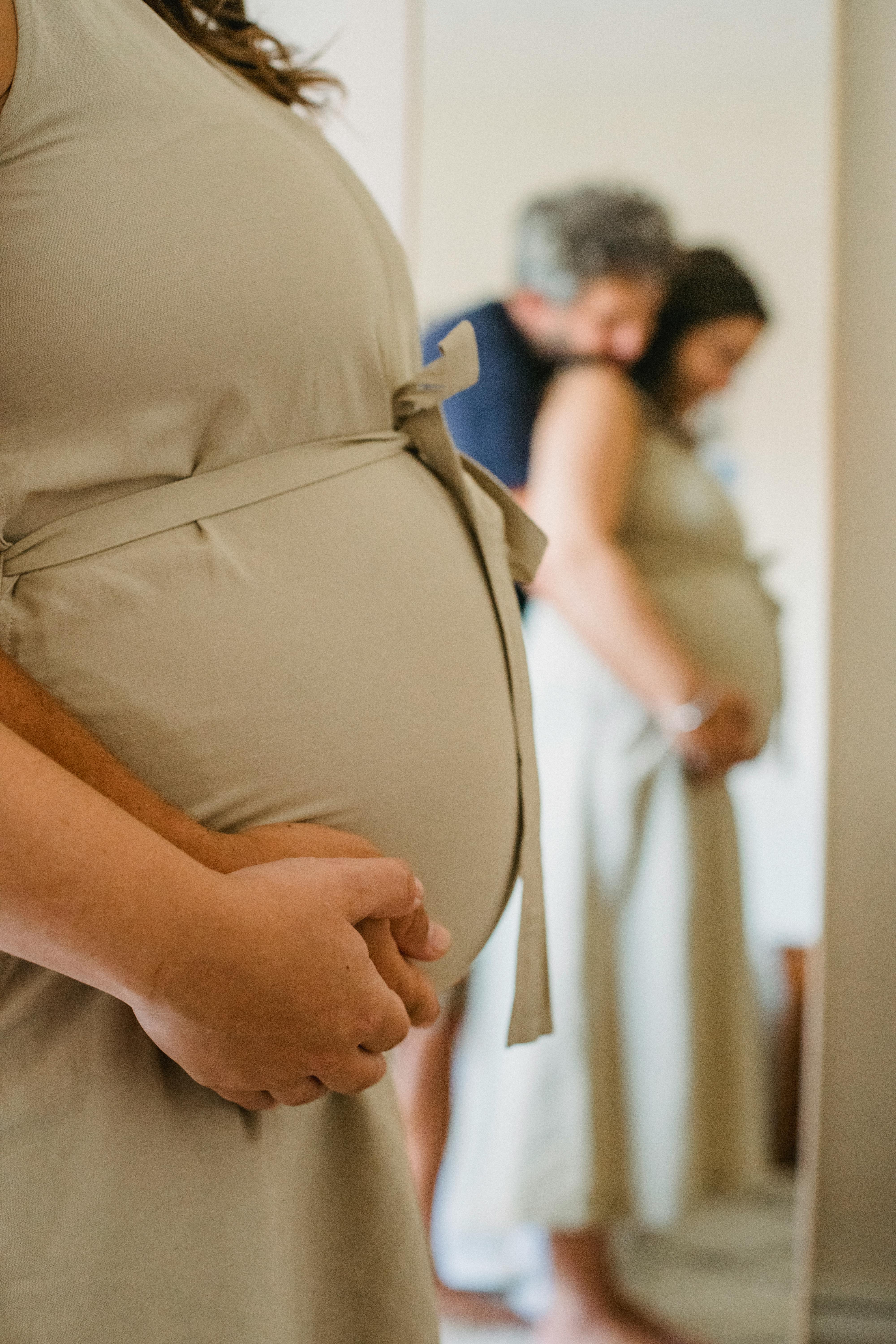 A pregnant couple embracing near a mirror | Source: Pexels