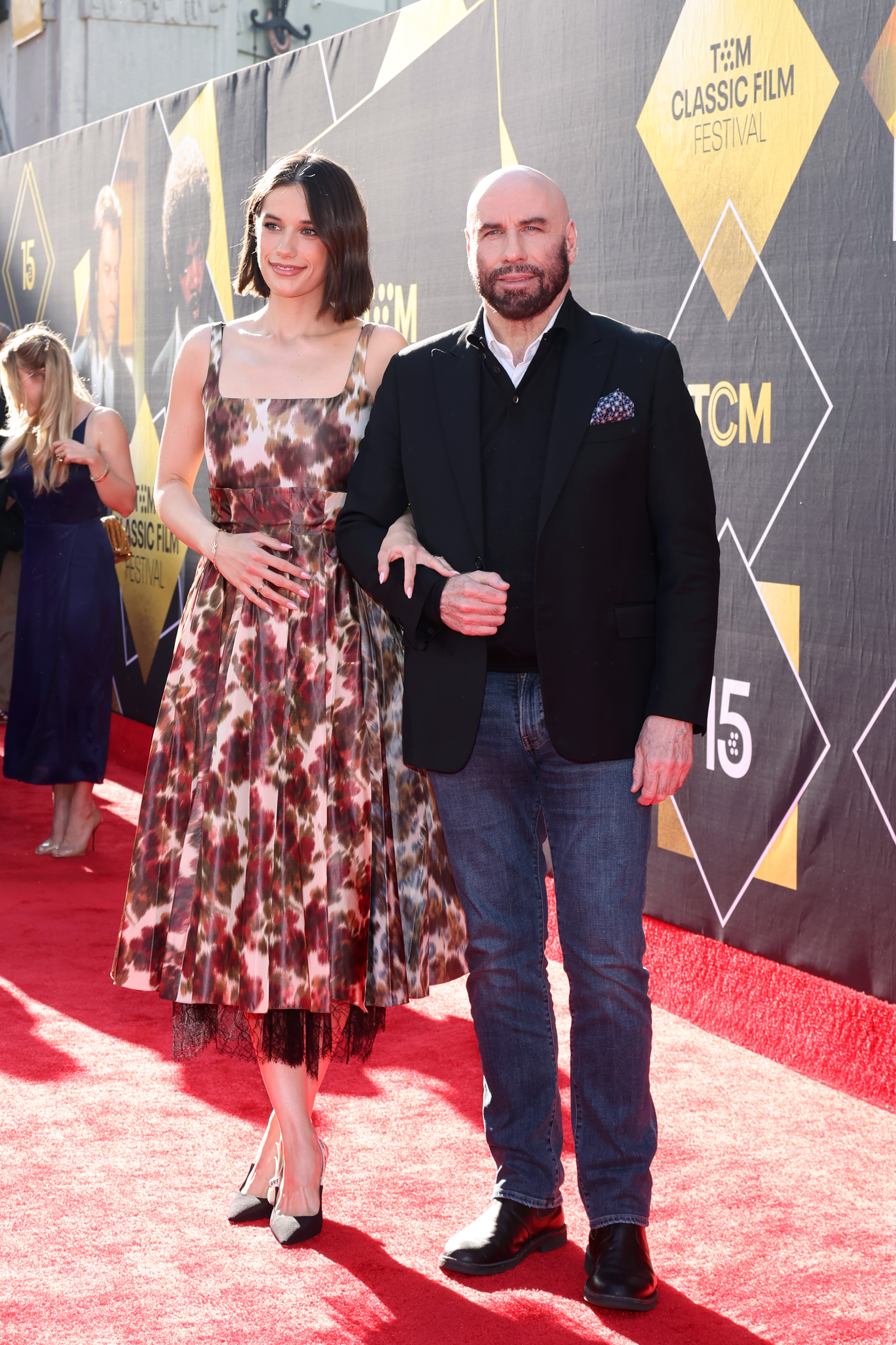 Ella Bleu Travolta stands beside John Travolta on the red carpet at the 2024 TCM Classic Film Festival. Her patterned dress and his dark blazer made for an elegant father-daughter moment celebrating the 30th Anniversary presentation of  "Pulp Fiction."
