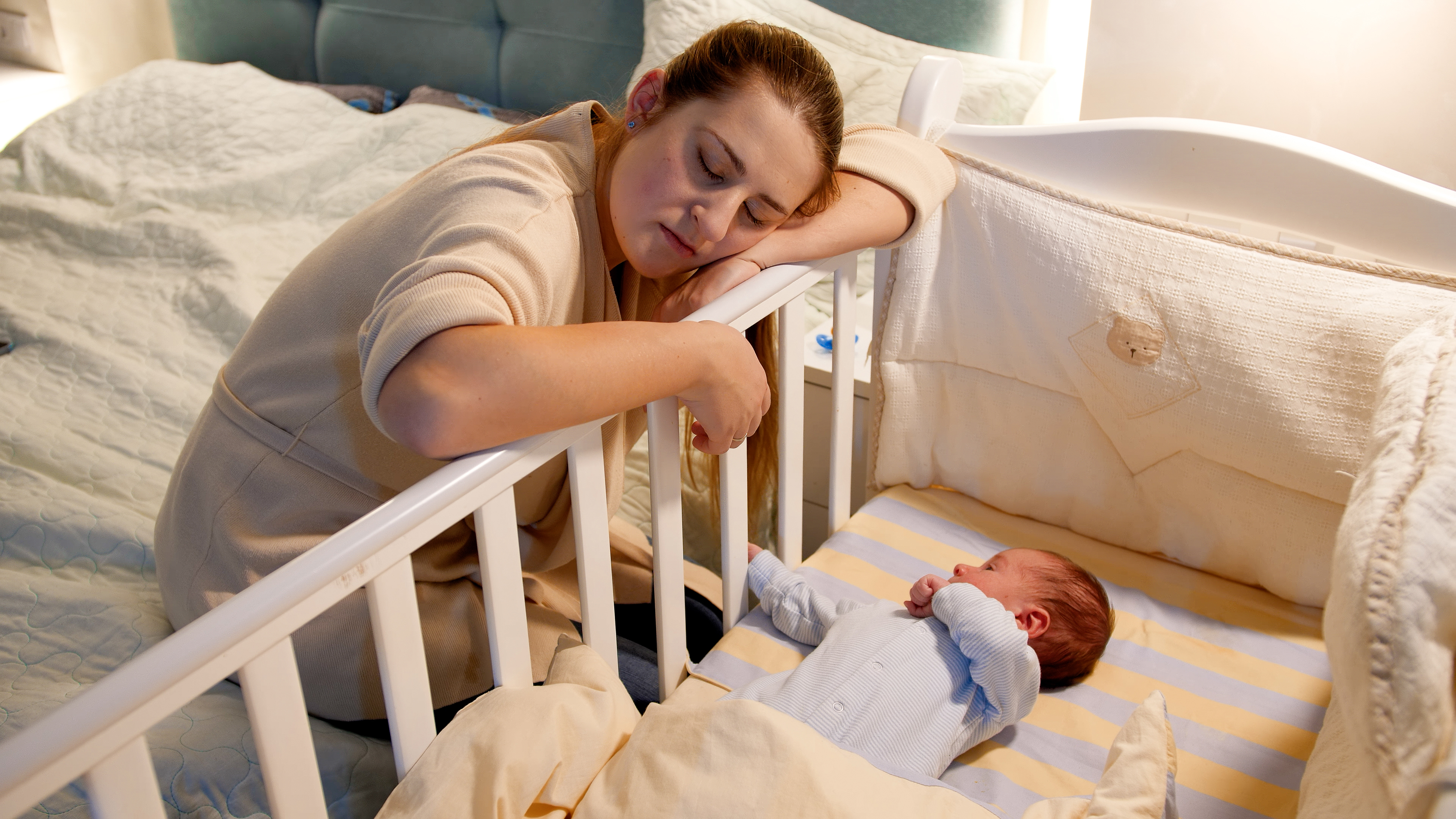 Tired mother sleeping by her child's crib | Source: Shutterstock