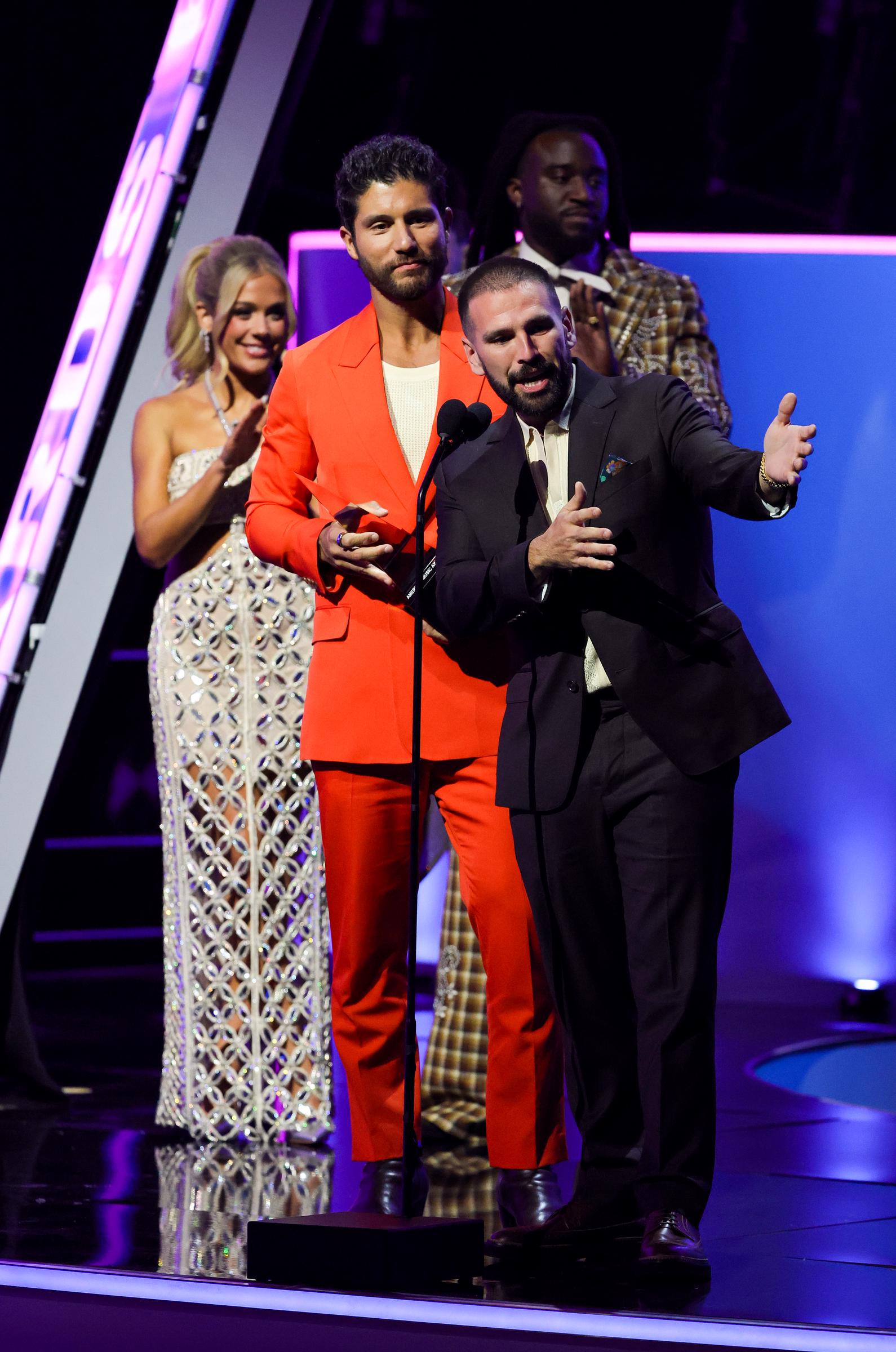 Framed by stage lights, she applauds behind the mic alongside Shaboozy as Dan + Shay deliver their acceptance speech for the Favorite Country Duo or Group award.