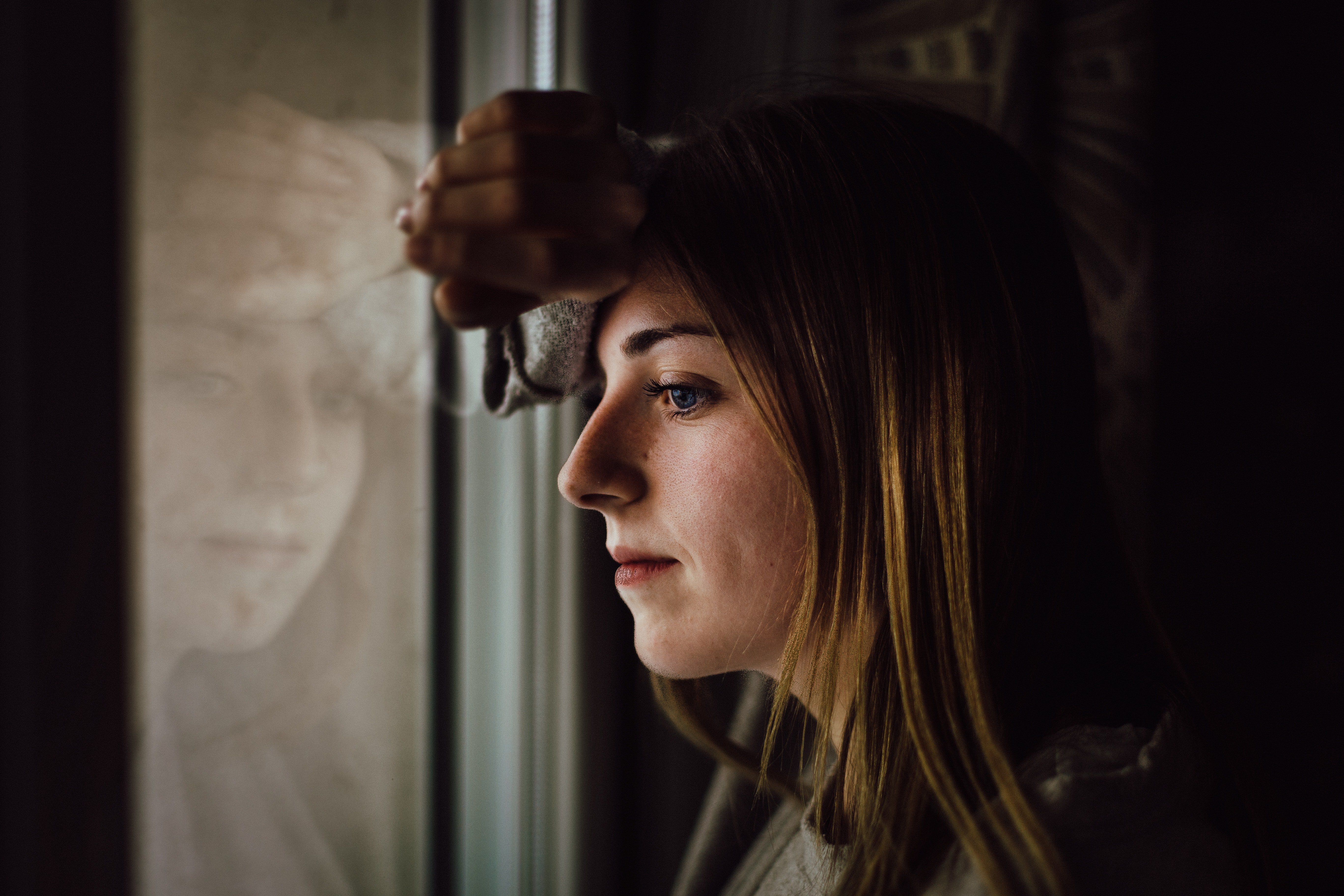 Una mujer con rostro angustiado mirando a través de una ventana. | Foto: Pexels