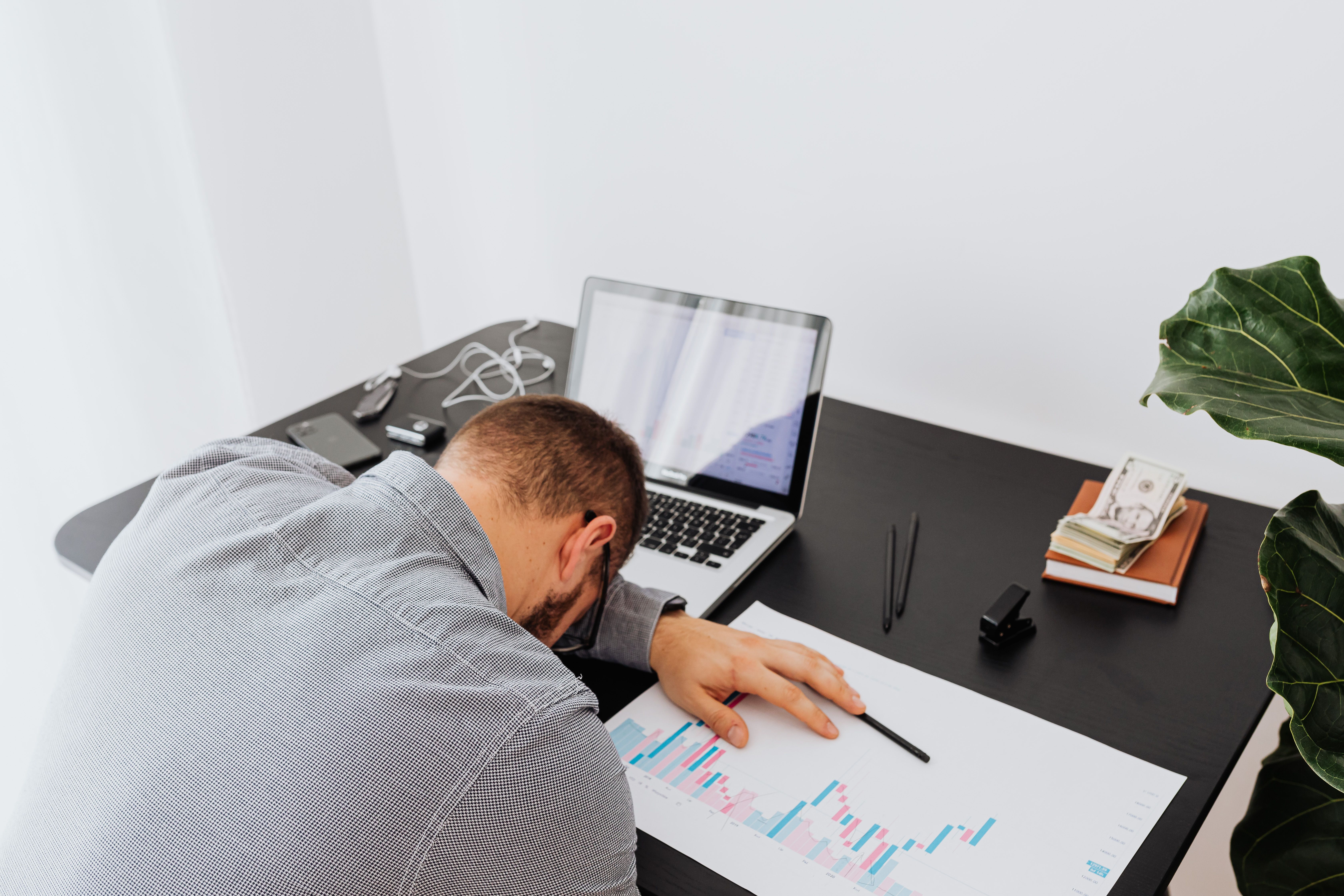 A man sitting at a desk with his head down next to a laptop and paperwork | Source: Pexels