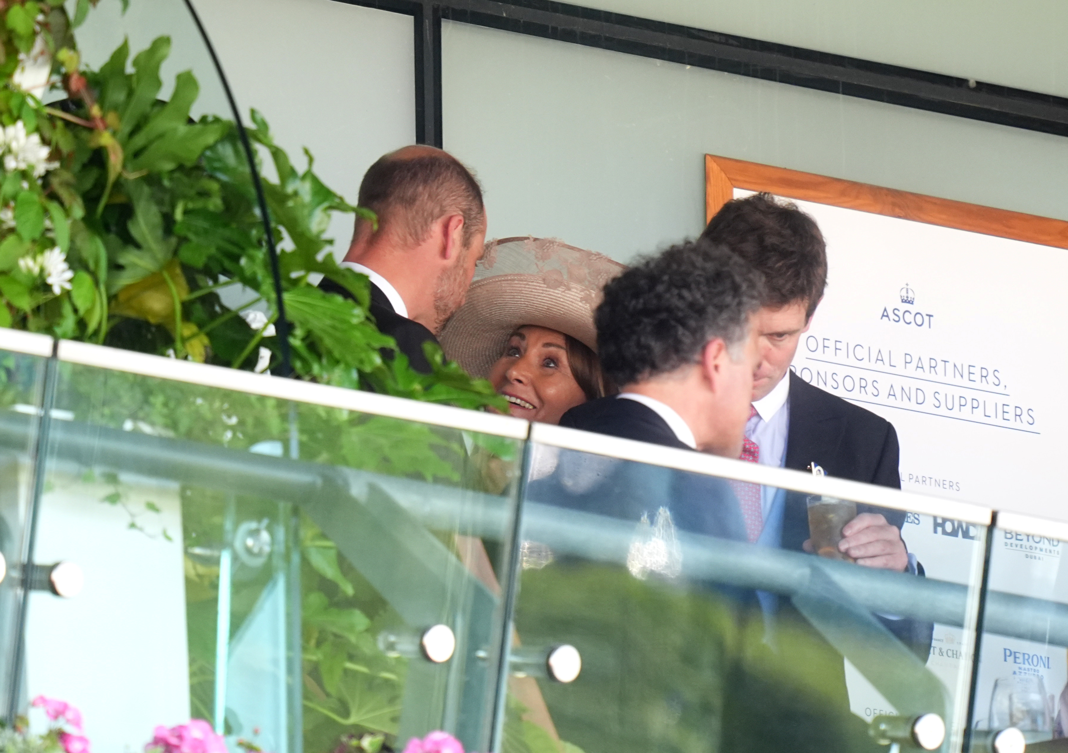 Prince William leans in as Carole Middleton looks up at him with a bright smile, sharing what appears to be an animated exchange amid a lively crowd in the royal box.