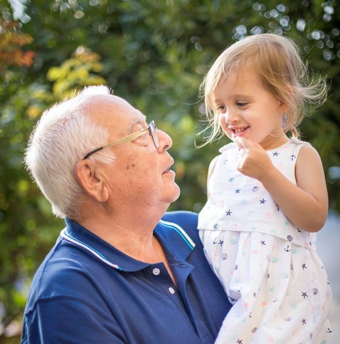 Un abuelo carga entre sus brazos a su nieta y la mira con amor. | Foto: Unsplash