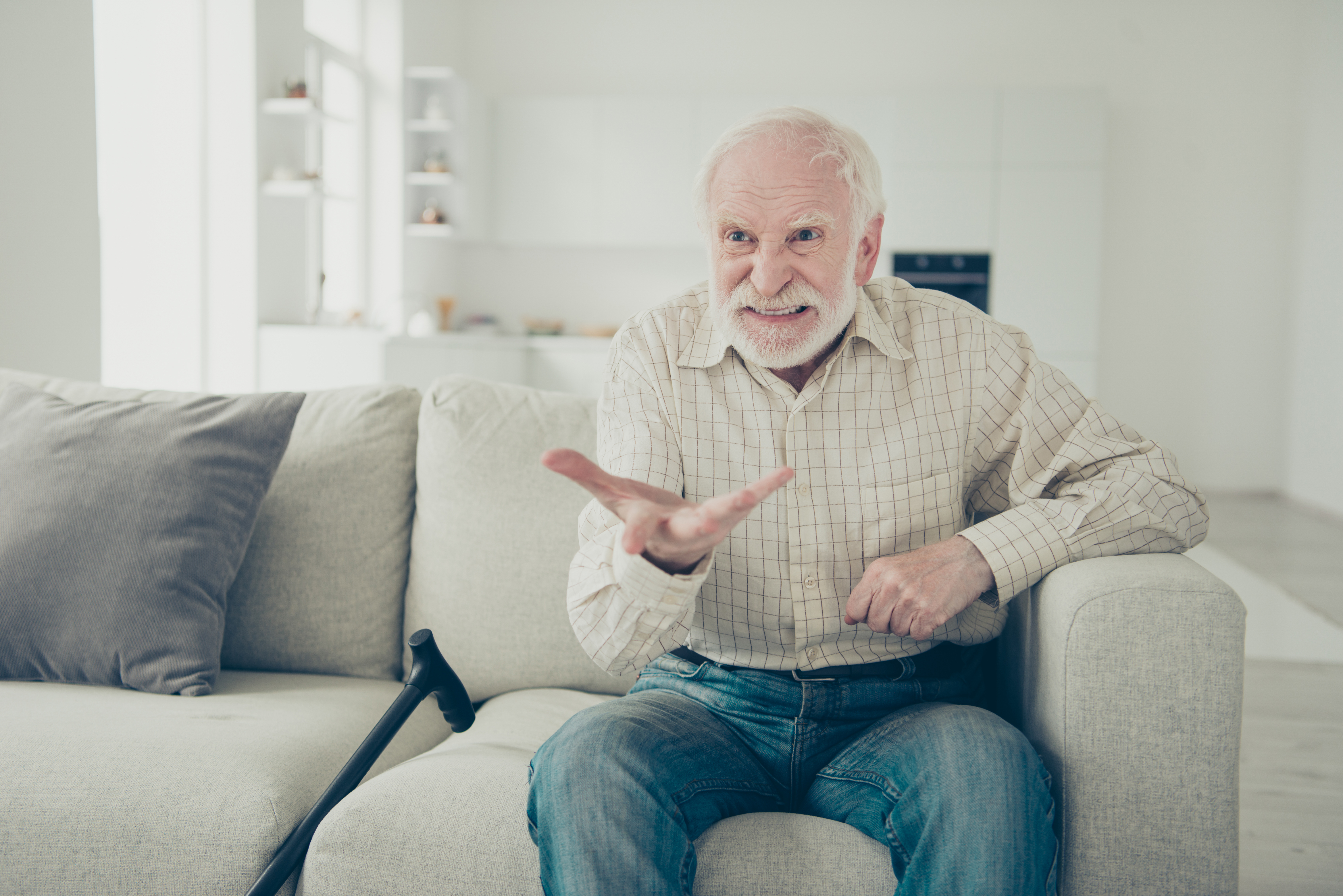 An elderly man arguing with someone not pictured while sitting on the sofa | Source: Shutterstock