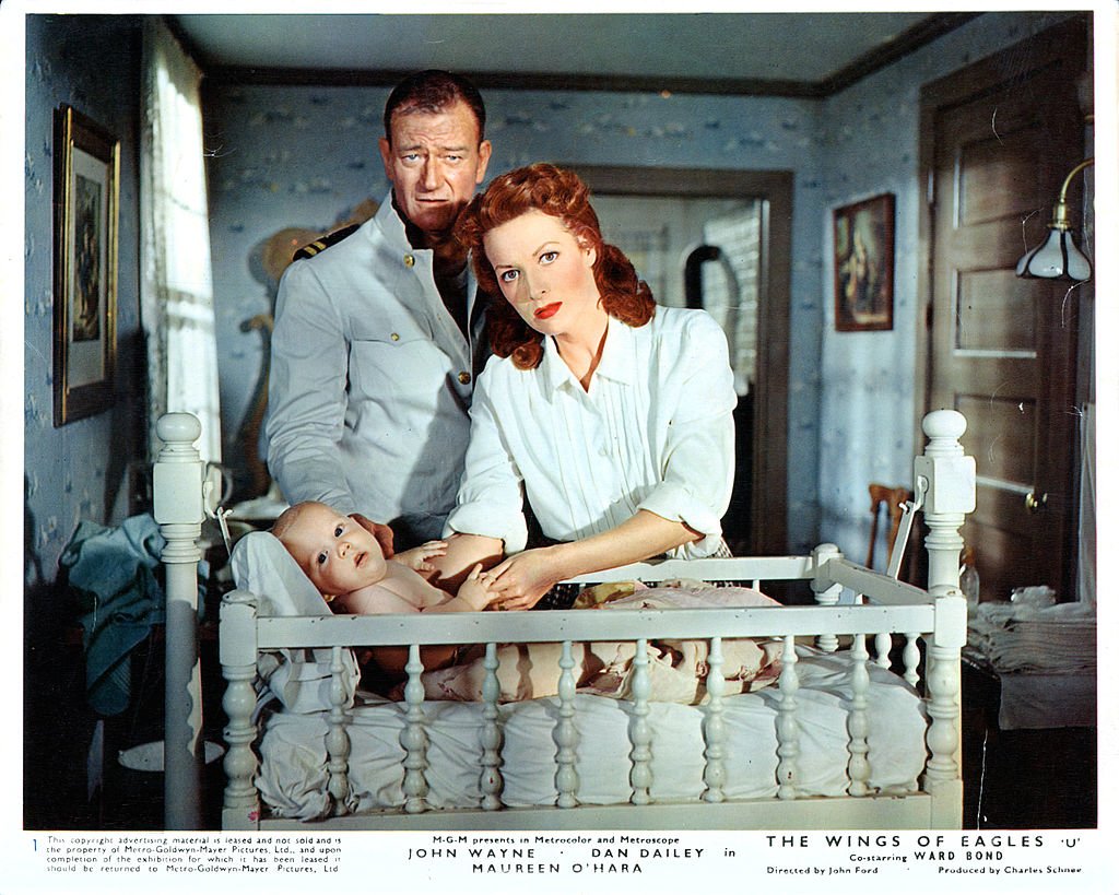 John Wayne and Maureen O'Hara stand over a baby in a crib in a scene from the film 'The Wings Of Eagles', 1957. | Source: Getty Images