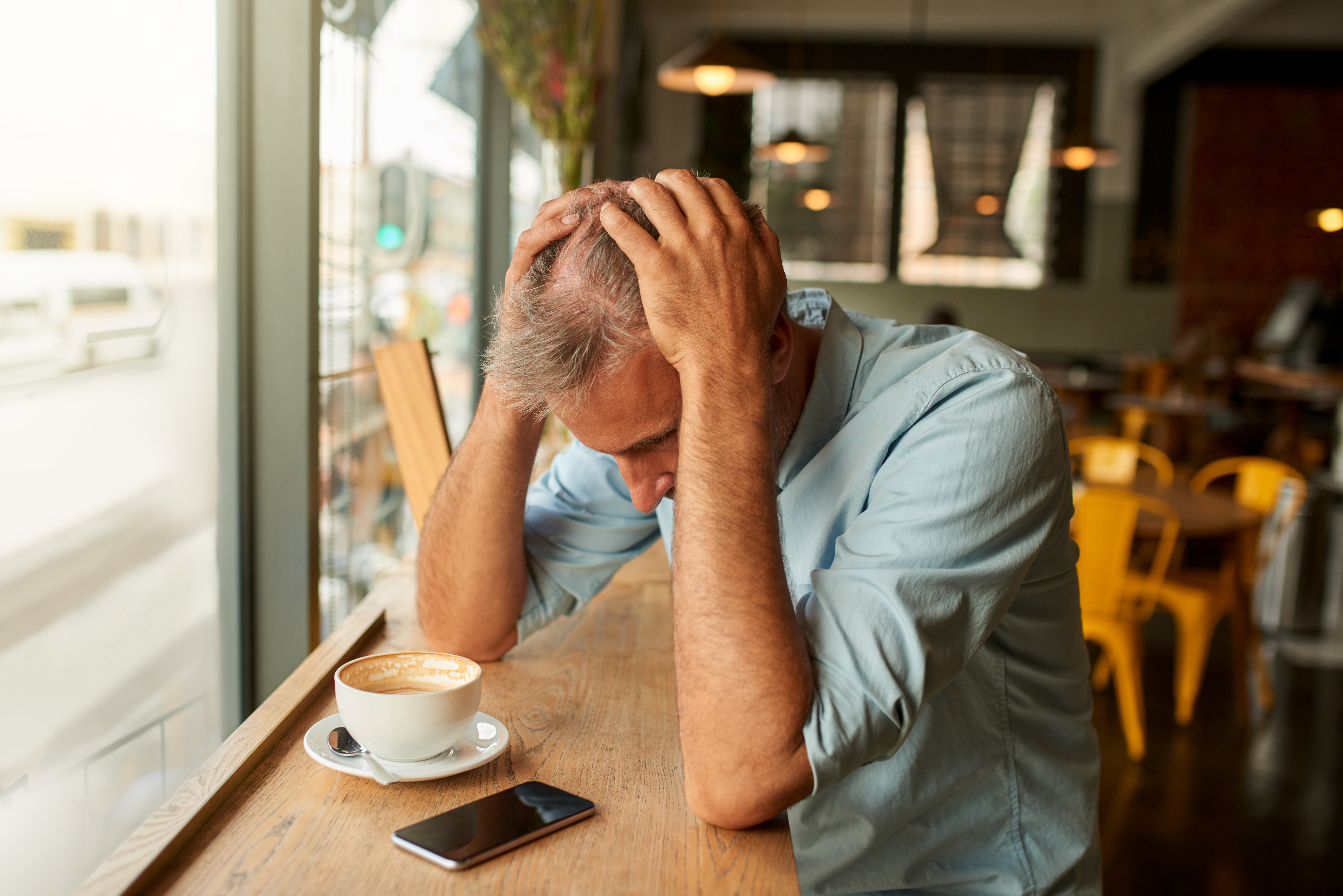 A stressed man looking at his mobile phone in a cafe | Source: Getty Images