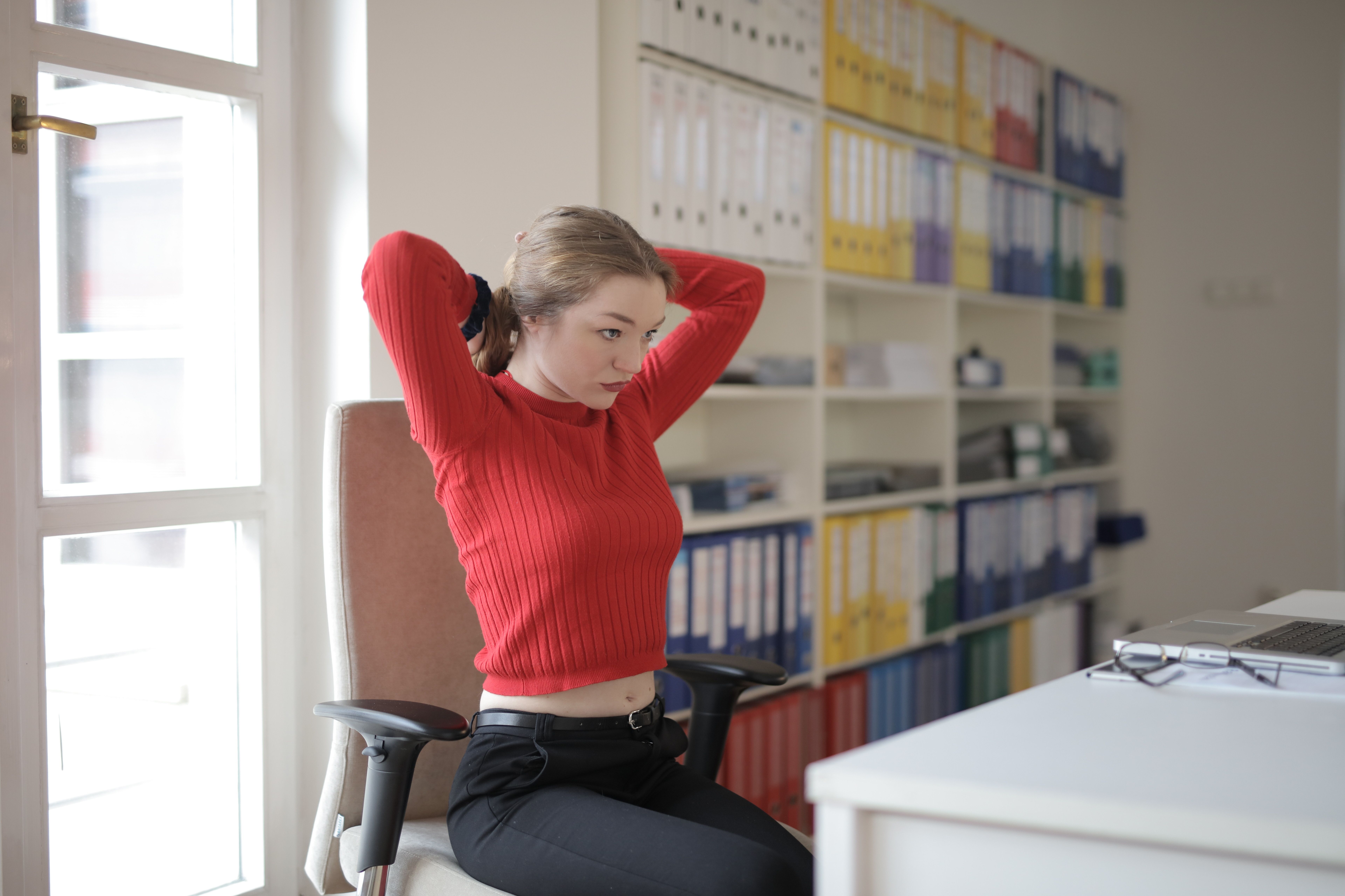 A woman stretches her arms behind her head while sitting in an office chair. | Source: Pexels