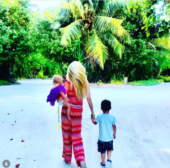Posted on 2 May 2019, Caroline Thomas is seen from behind walking along a sunlit, palm-lined path, gently carrying her young daughter while holding her son's hand — a serene and intimate glimpse into her life as a hands-on mother, far removed from the glare of television fame. | Source: Instagram/carolinethomas23