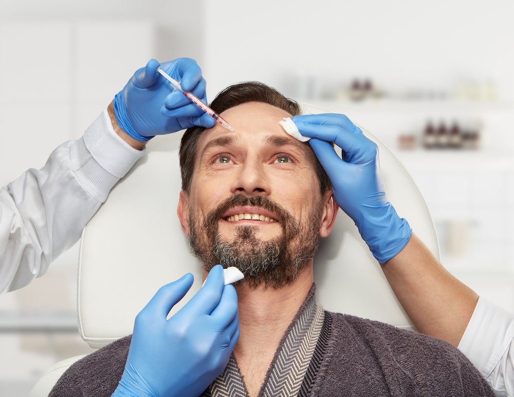 Hombre recostado recibiendo aplicación de bótox en la frente. | Foto: Shutterstock