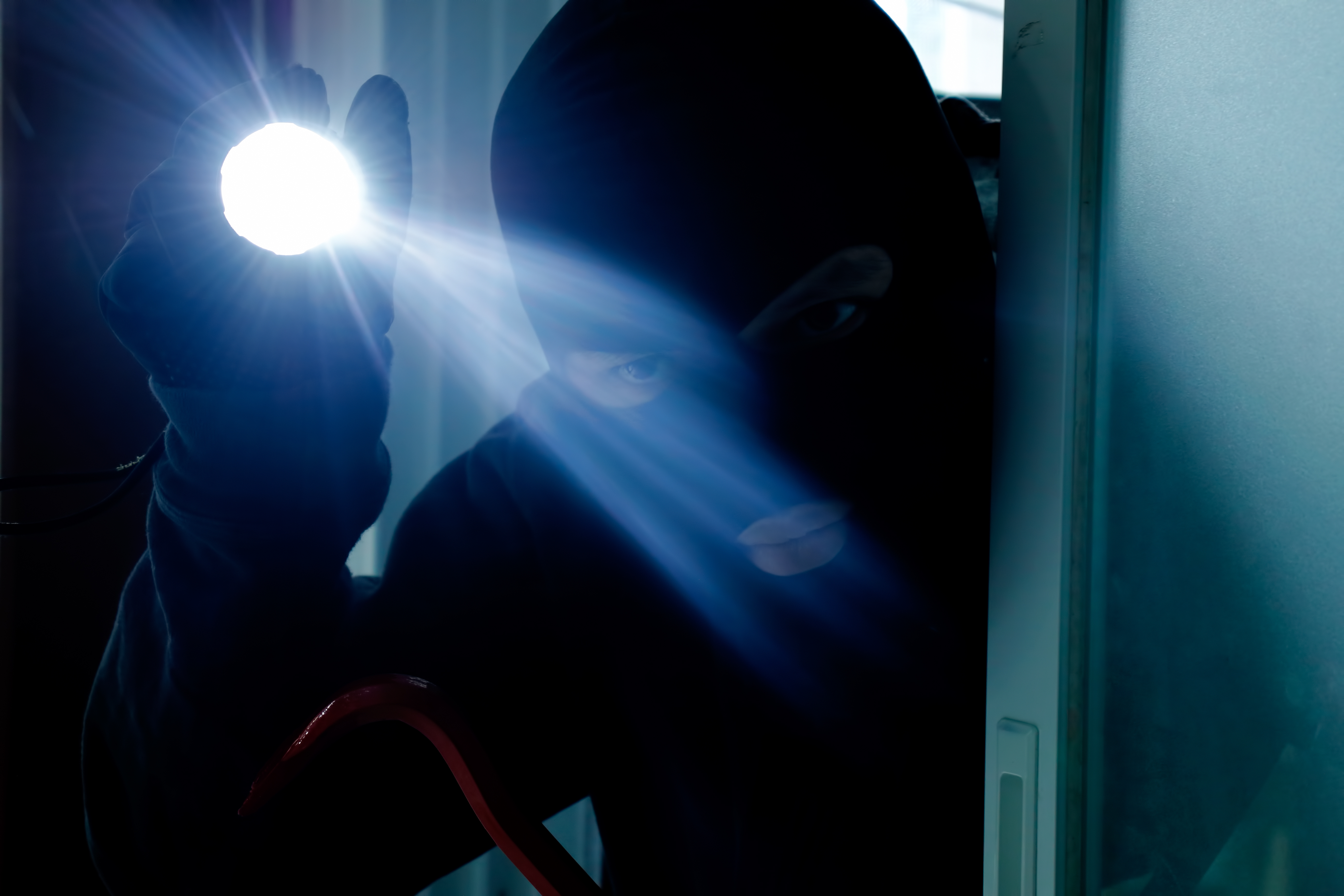 Masked burglar holding flashlight while secretly entering into a house | Source: Getty Images