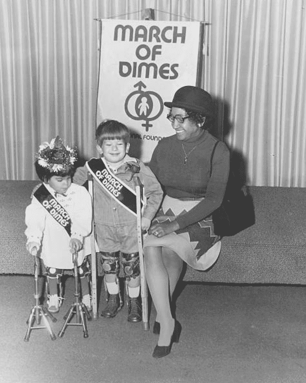 A March of Dimes fund raising event with woman on a stage sitting with two children holding crutches, in 1970 | Source: Getty Images