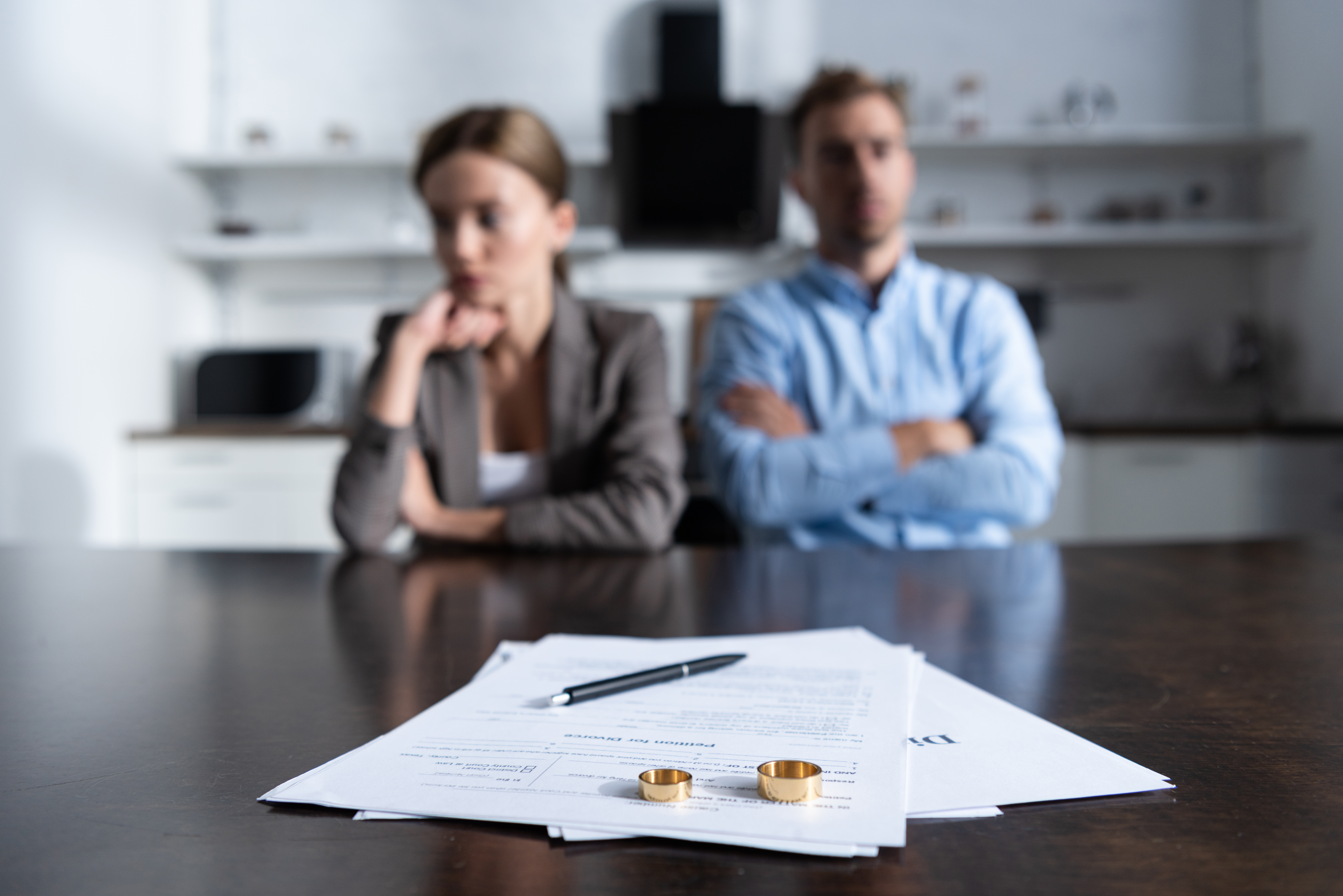 An upset couple sitting in the background with divorce papers and their rings on a table | Source: Shutterstock