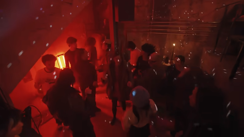 An overhead view shows partygoers gathering under the stairs on the red-lit dance floor as light reflects from a vintage disco ball. | Source: YouTube/@Archdigest