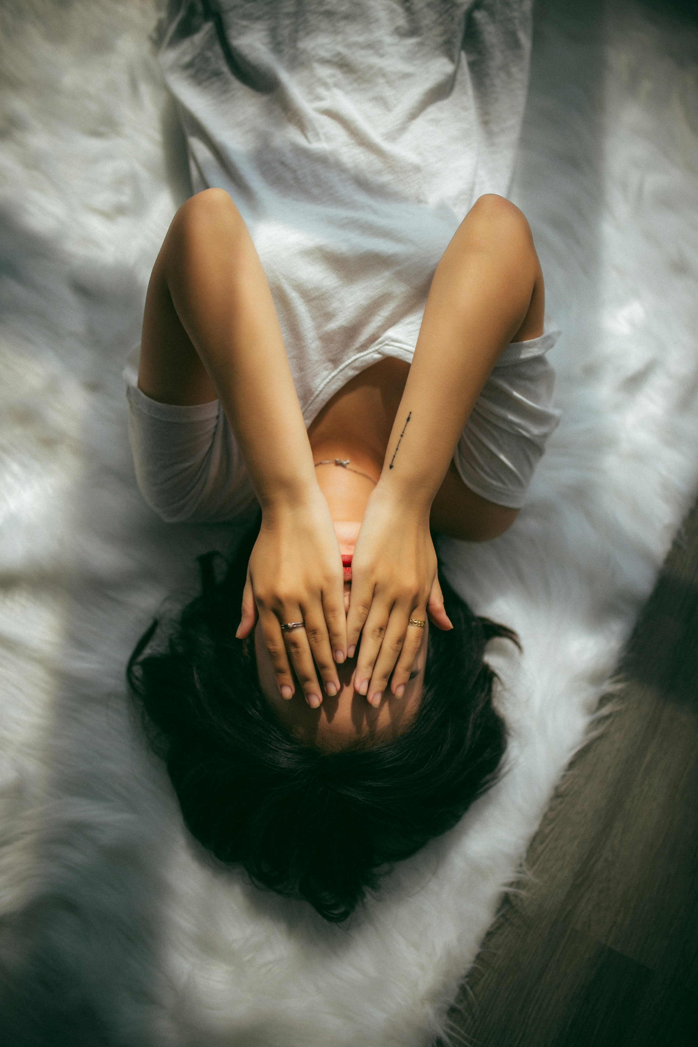 A woman lying across the bed hiding her face | Souce: Unsplash
