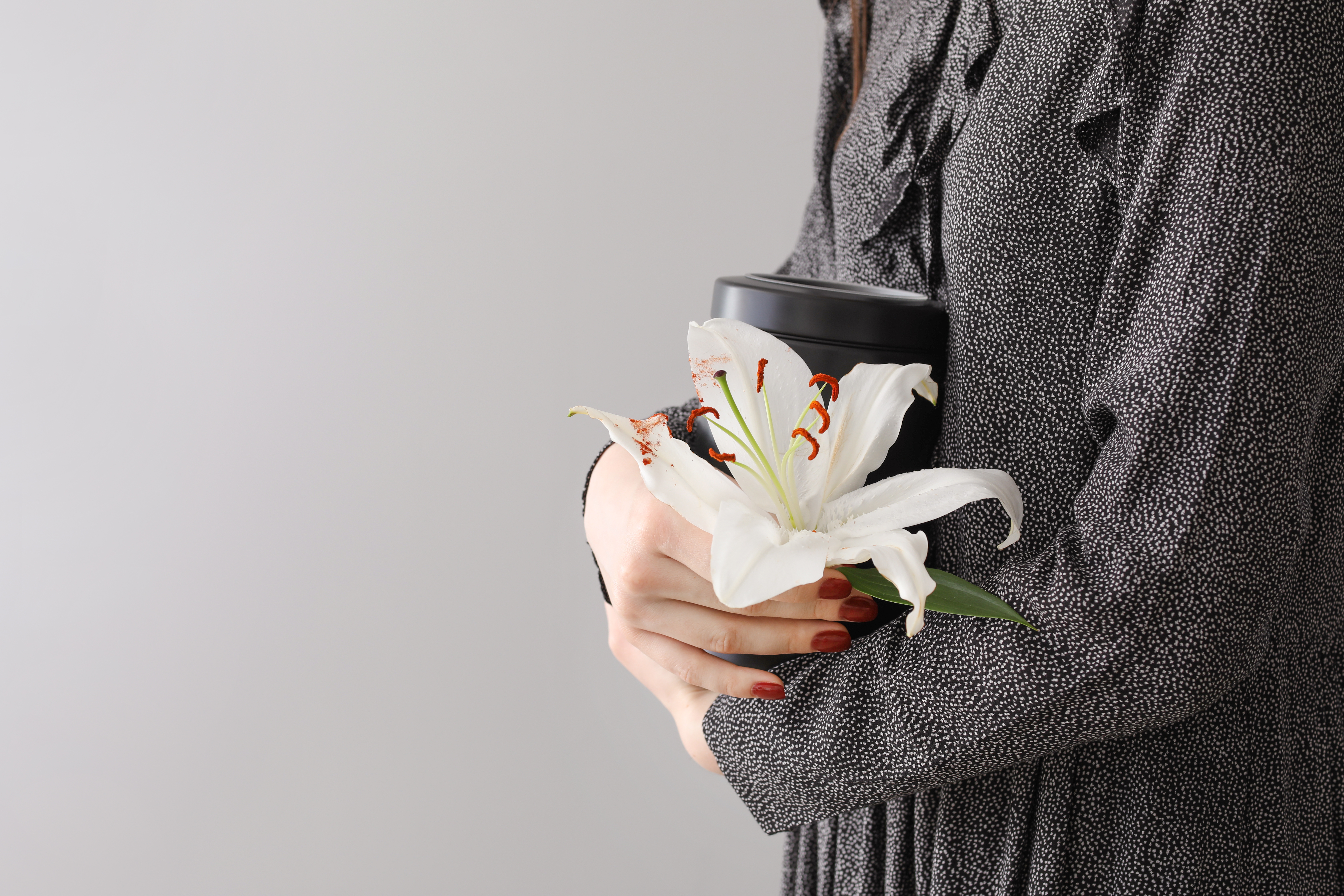 A woman is seen holding a mortuary urn and a white lily flower | Source: Shutterstock
