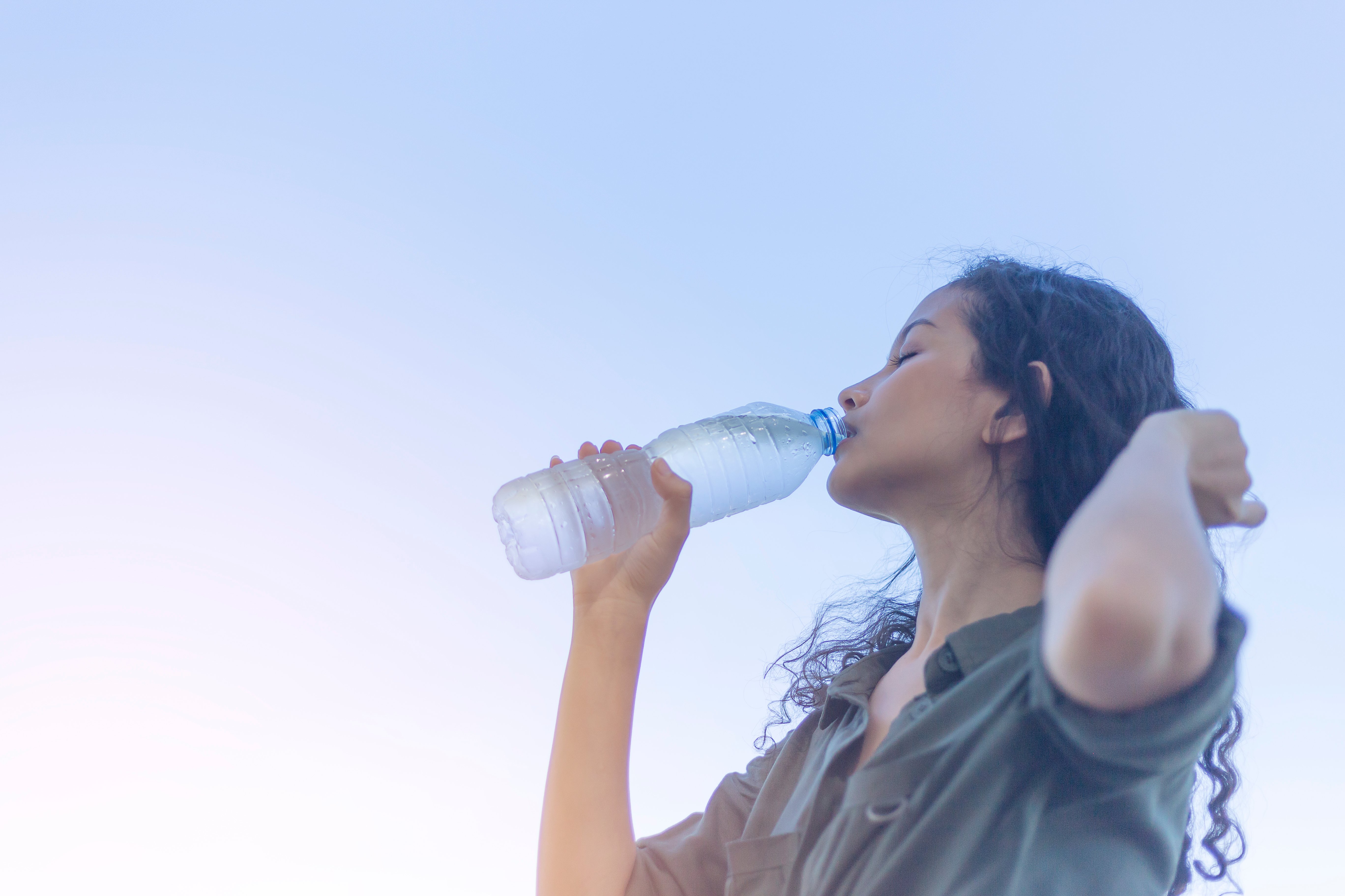 Joyeuse femme buvant de l'eau avec une bouteille en plastique dans la main. | Photo : Shutterstock