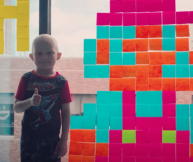 A boy battling cancer smiles as he stands next to his creative Post-it note art | Photo: Youtube/Good Morning America