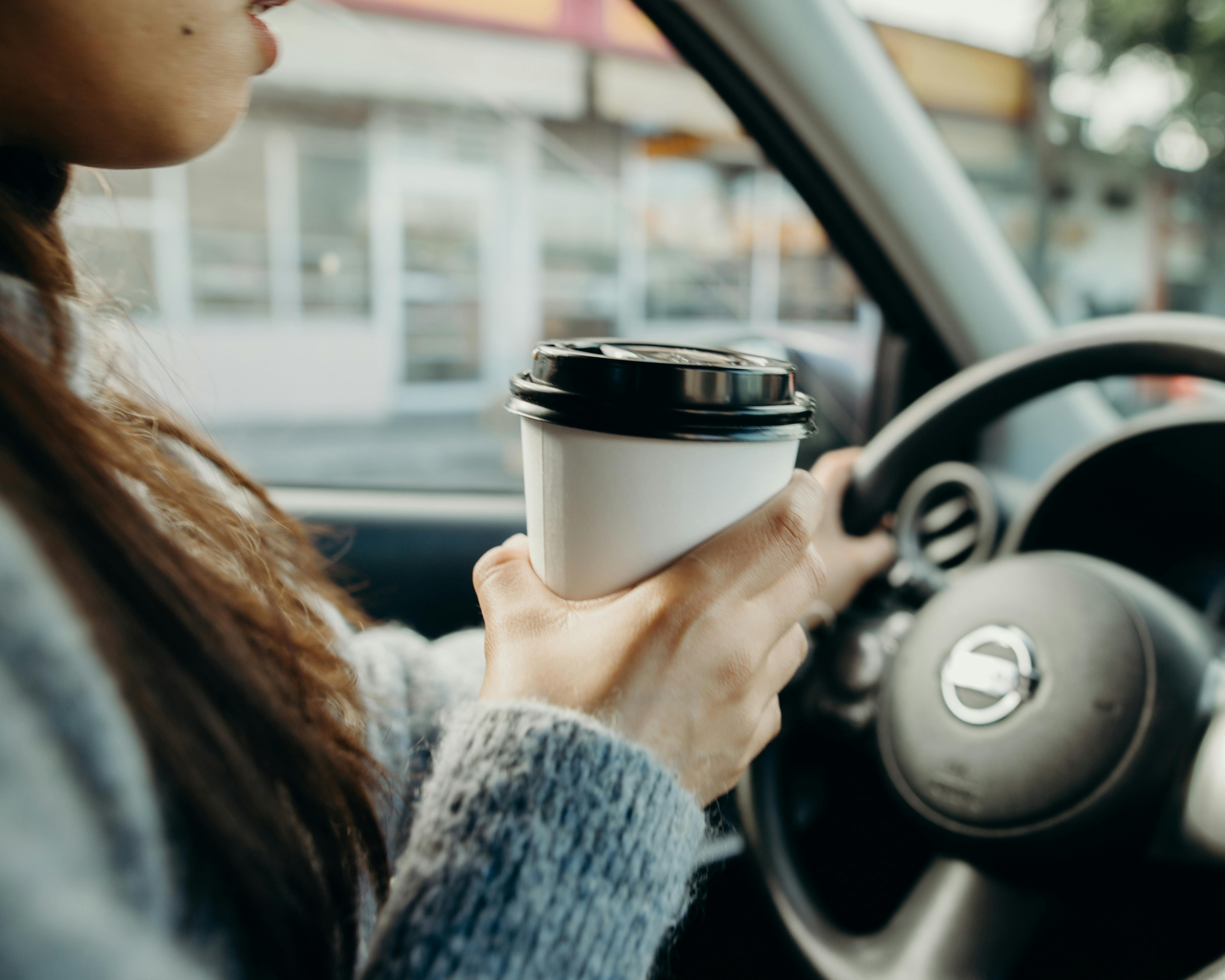 A woman driving while holding coffee | Source: Pexels