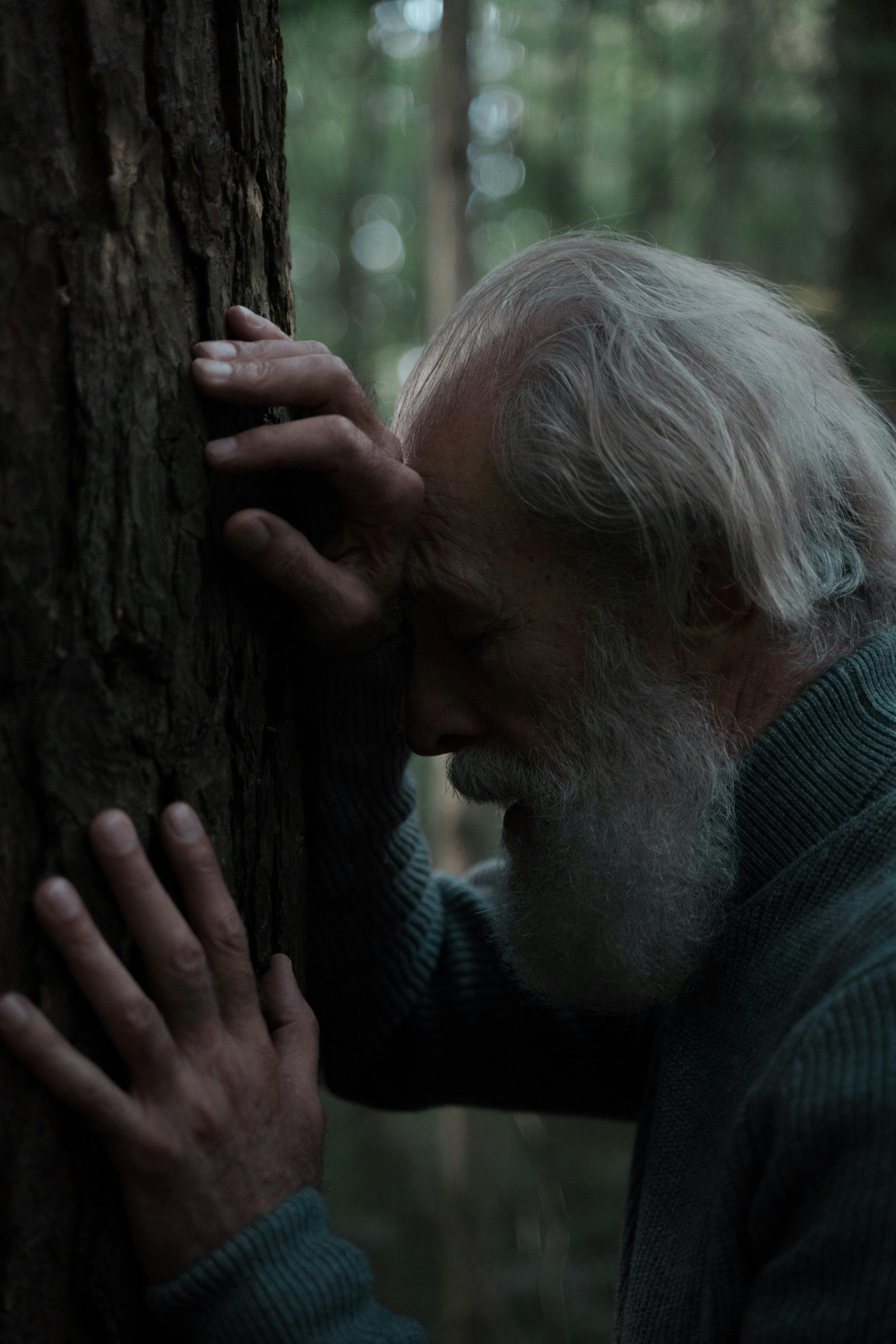 A sad man leaning against a tree trunk | Source: Pexels