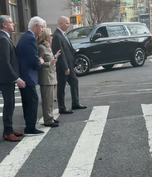 Hillary Clinton raises her hands as she and Bill Clinton stand with aides and security at a zebra-striped crosswalk on the busy Manhattan intersection. | Source: TikTok/elderordonez