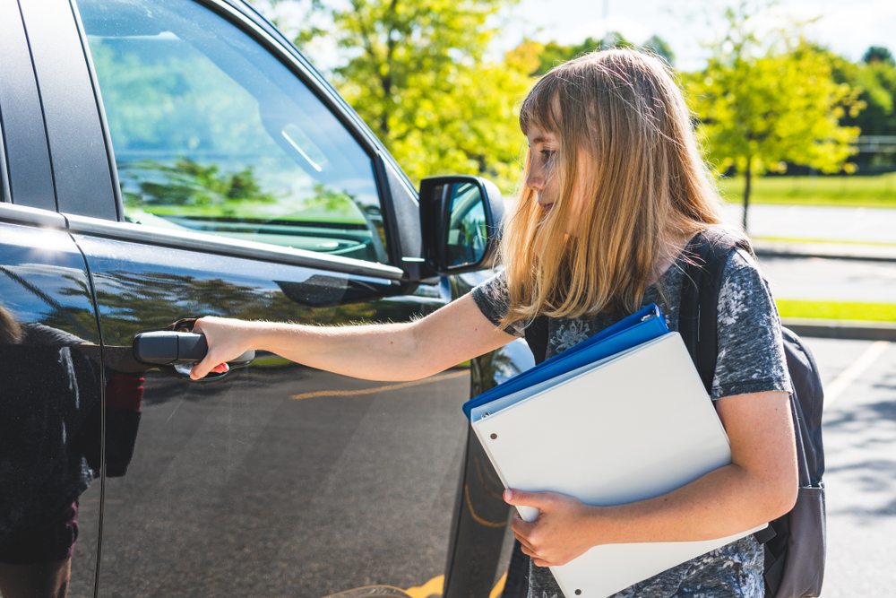 A teenage girl standing beside a car | Source: Shutterstock