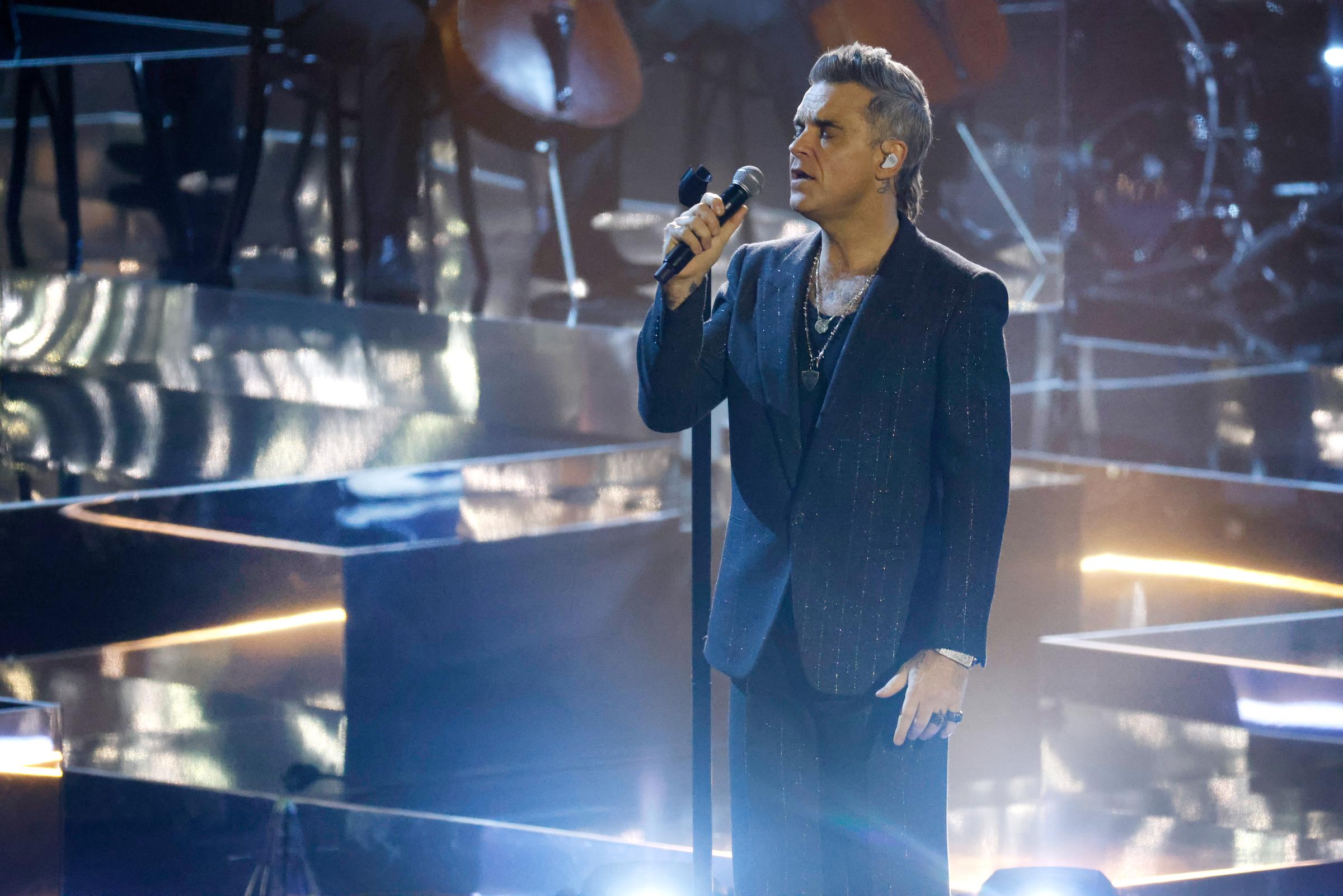 Robbie Williams performed live in 2022, dressed in a dark, shimmering suit with layered necklaces. Commanding the stage with a soulful expression, the pop veteran delivered a performance that blended elegance with emotional depth.