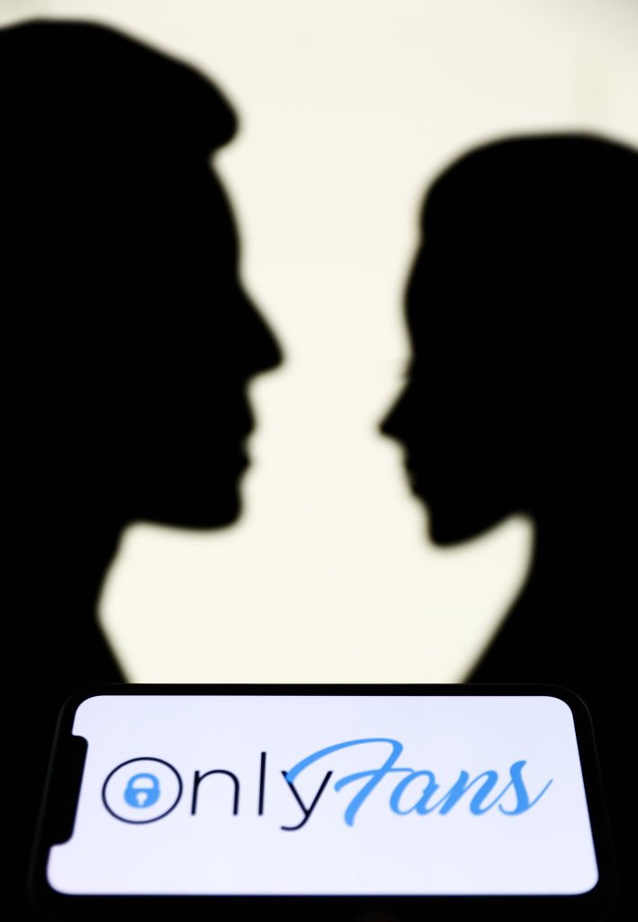 OnlyFans logo displayed on a phone screen is seen with paper silhouettes looking like a man and a woman in the background in this illustration photo taken in Krakow, Poland on August 25, 2021. | Source: Getty Images