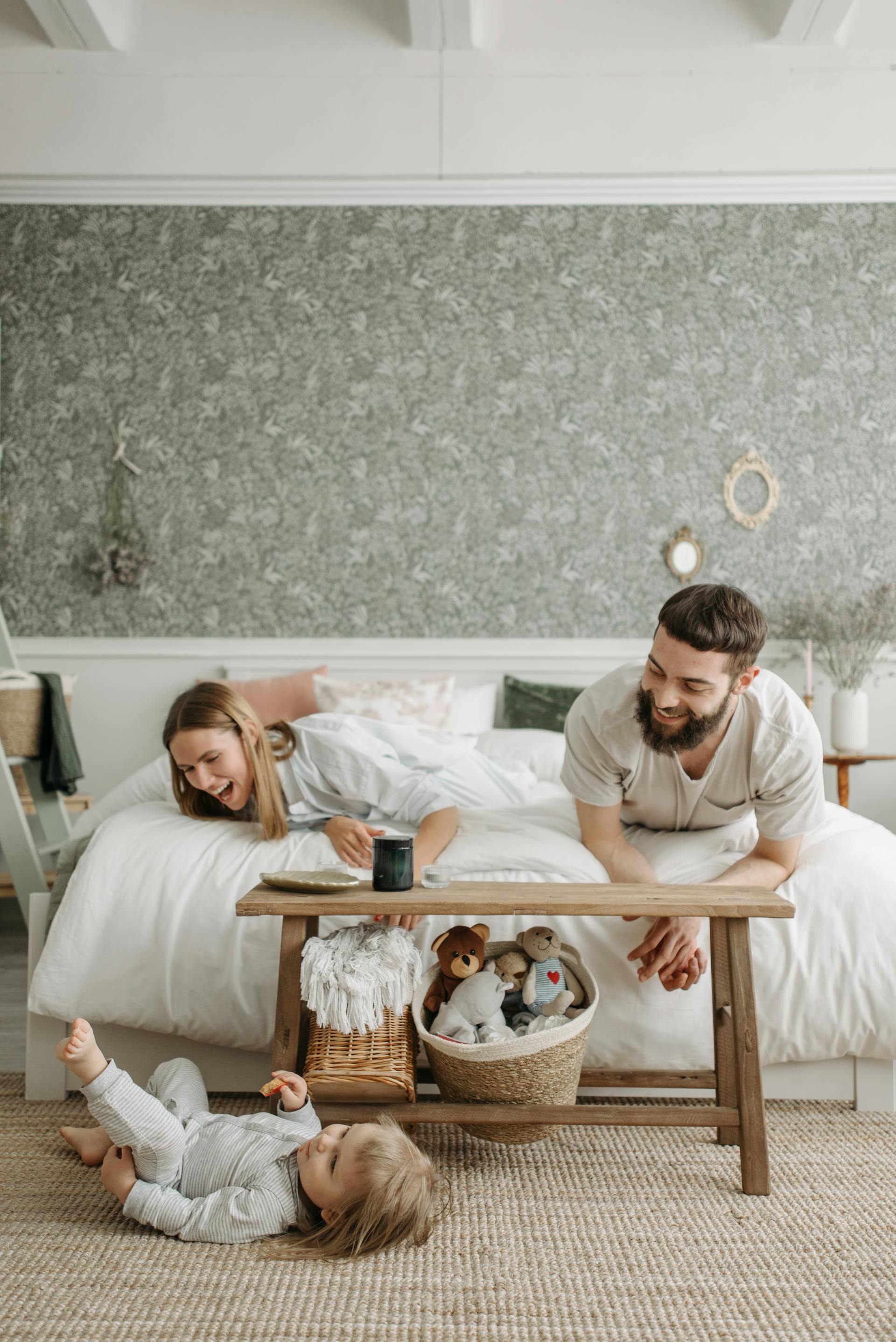 A couple lying on the bed watching their little daughter playing on the floor | Source: Pexels