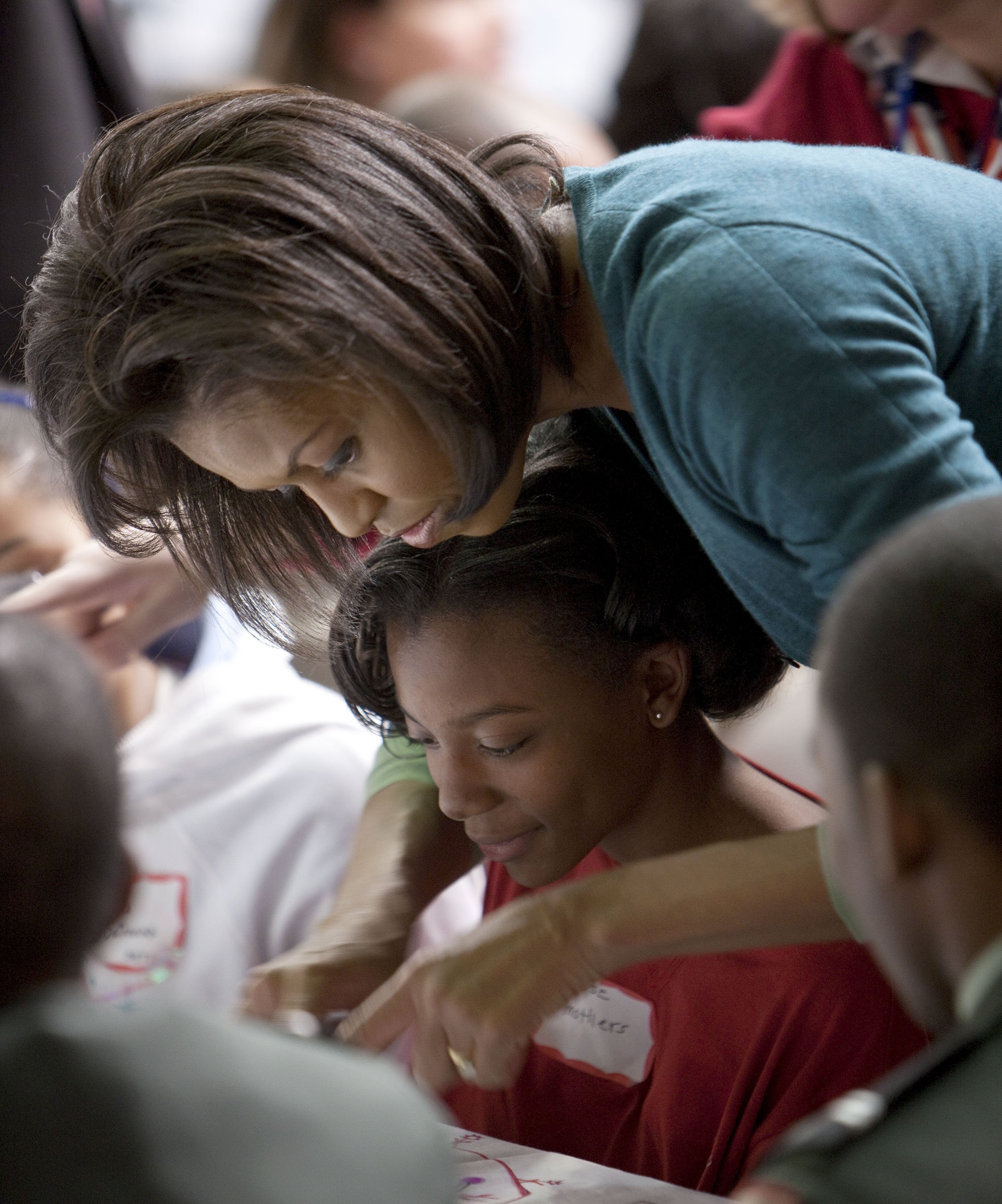 Michelle Obama helps a girl at Calvin Coolidge High School where students, military families, and volunteer service groups are working on various projects supporting the troops on January 19, 2009, in Washington, DC. | Source: Getty Images.