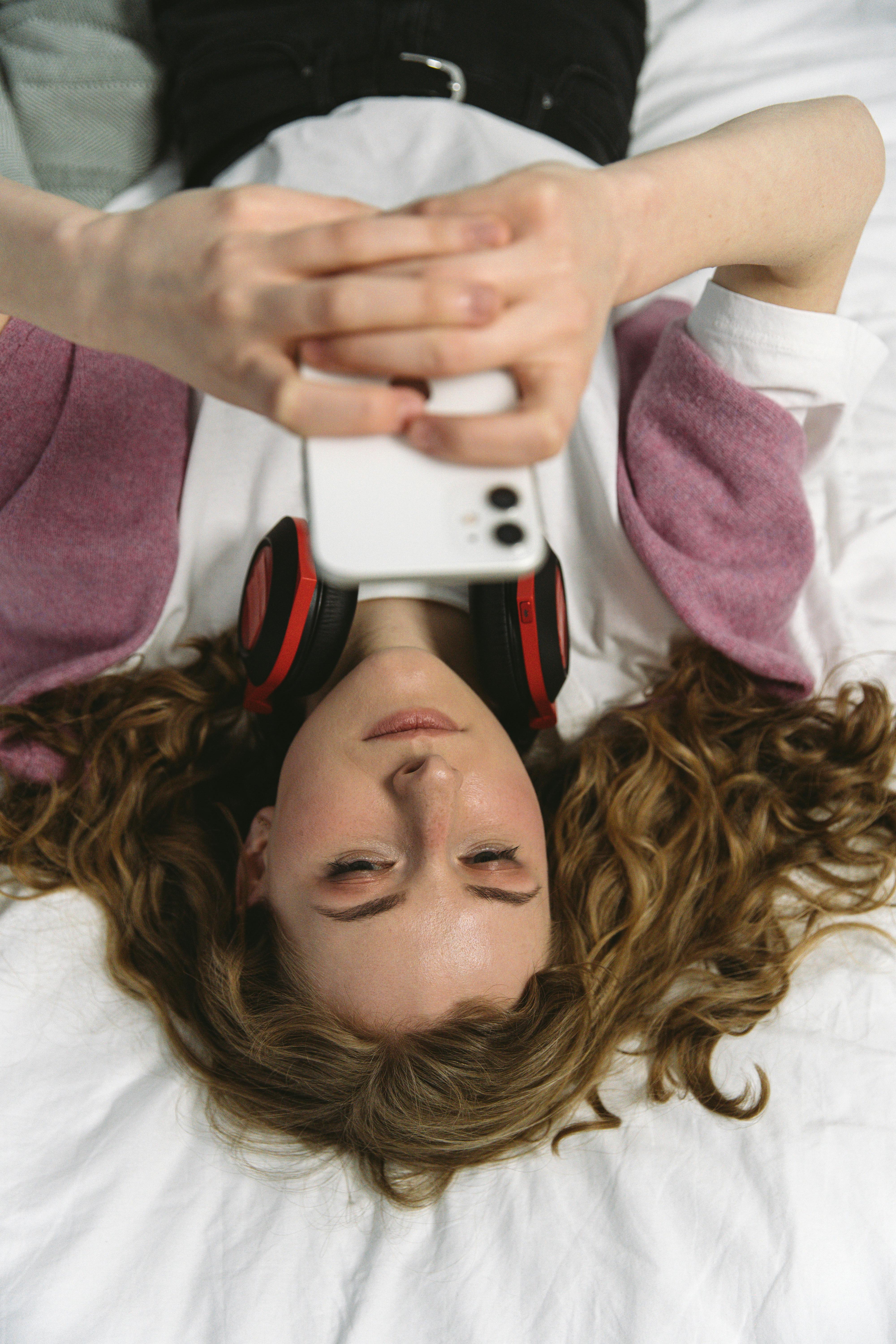 A woman using her phone while lying on a bed | Source: Pexels