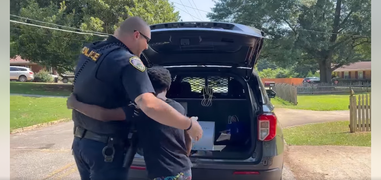 Officer Colleran wird von einem Jungen umarmt, nachdem er ihn zum Kofferraum seines Autos gebracht hat, um ihm etwas zu zeigen, nachdem Leute aus der Nachbarschaft die Polizei auf das Kind angesetzt hatten, am 24. Juli 2023 | Quelle: Facebook/City of Hapeville Police