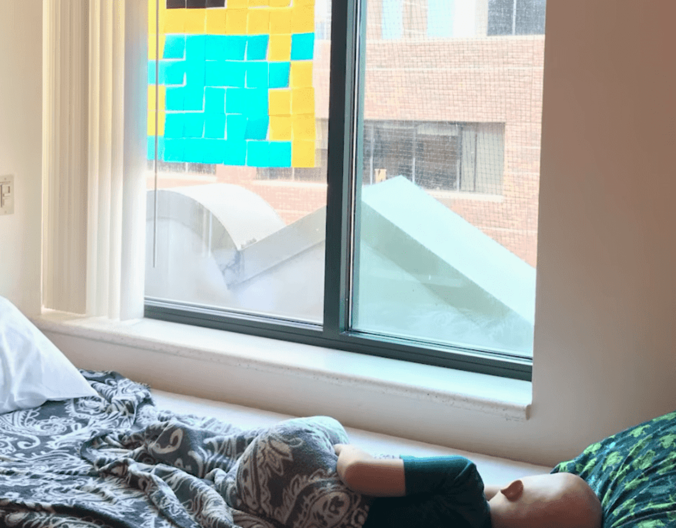 A boy battling cancer lies next to his creative Post-it note art | Photo: Youtube/Good Morning America