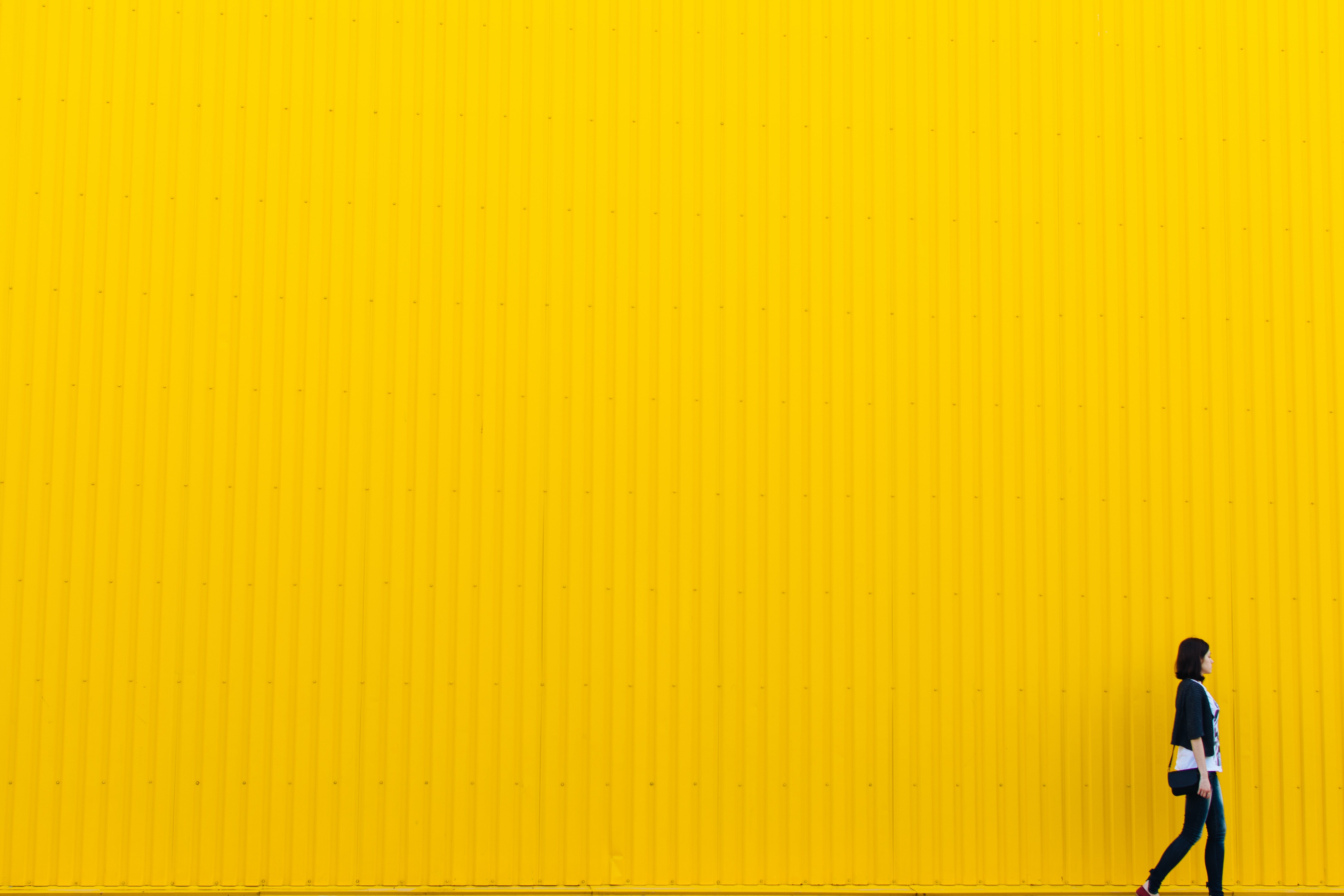 A woman walking in front of a yellow background. │Source: Unsplash